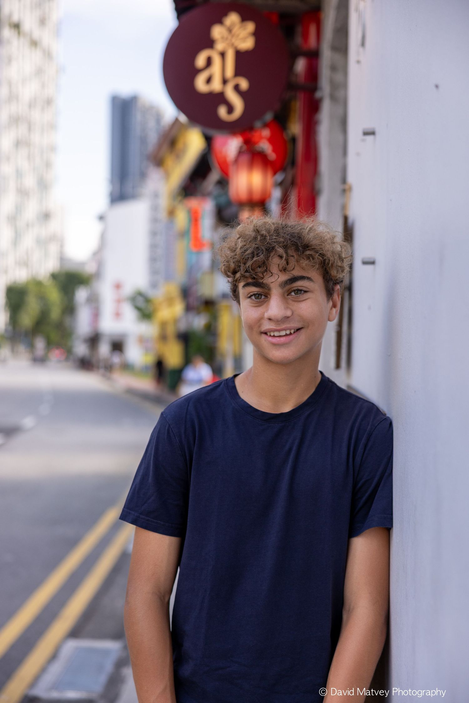 Smiling teenage boy in navy t-shirt posing on a vibrant Chinatown street sidewalk.