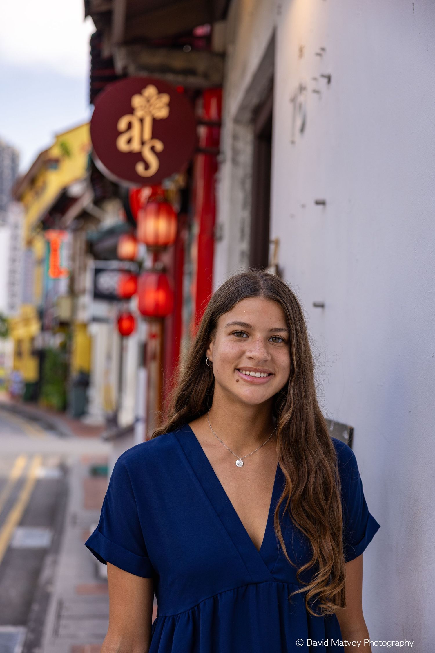 Young woman in blue dress smiling on a colorful street in Singapore's Chinatown with red lanterns.