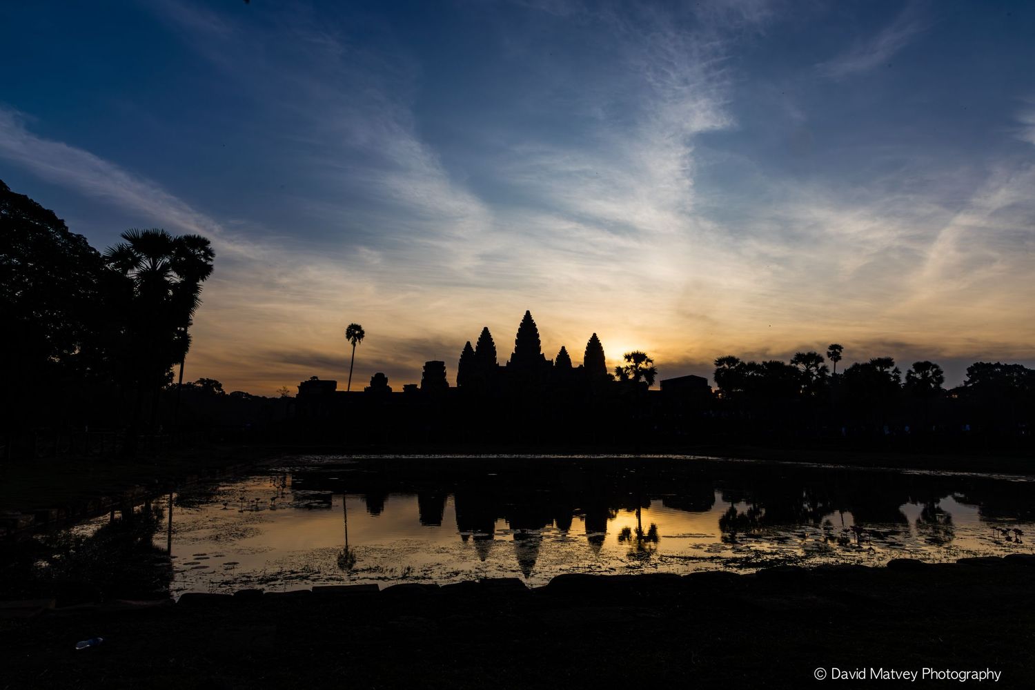 Silhouette of Angkor Wat temple reflected in still water at dawn with colorful sky.