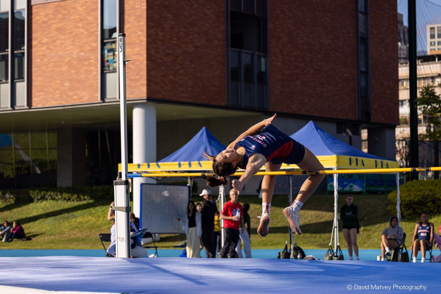 High jumper arches over bar using Fosbury Flop technique at outdoor athletics competition.