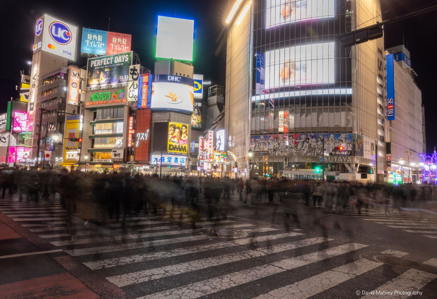 Long exposure shot of crowds crossing the famous Shibuya intersection surrounded by neon signs at night.