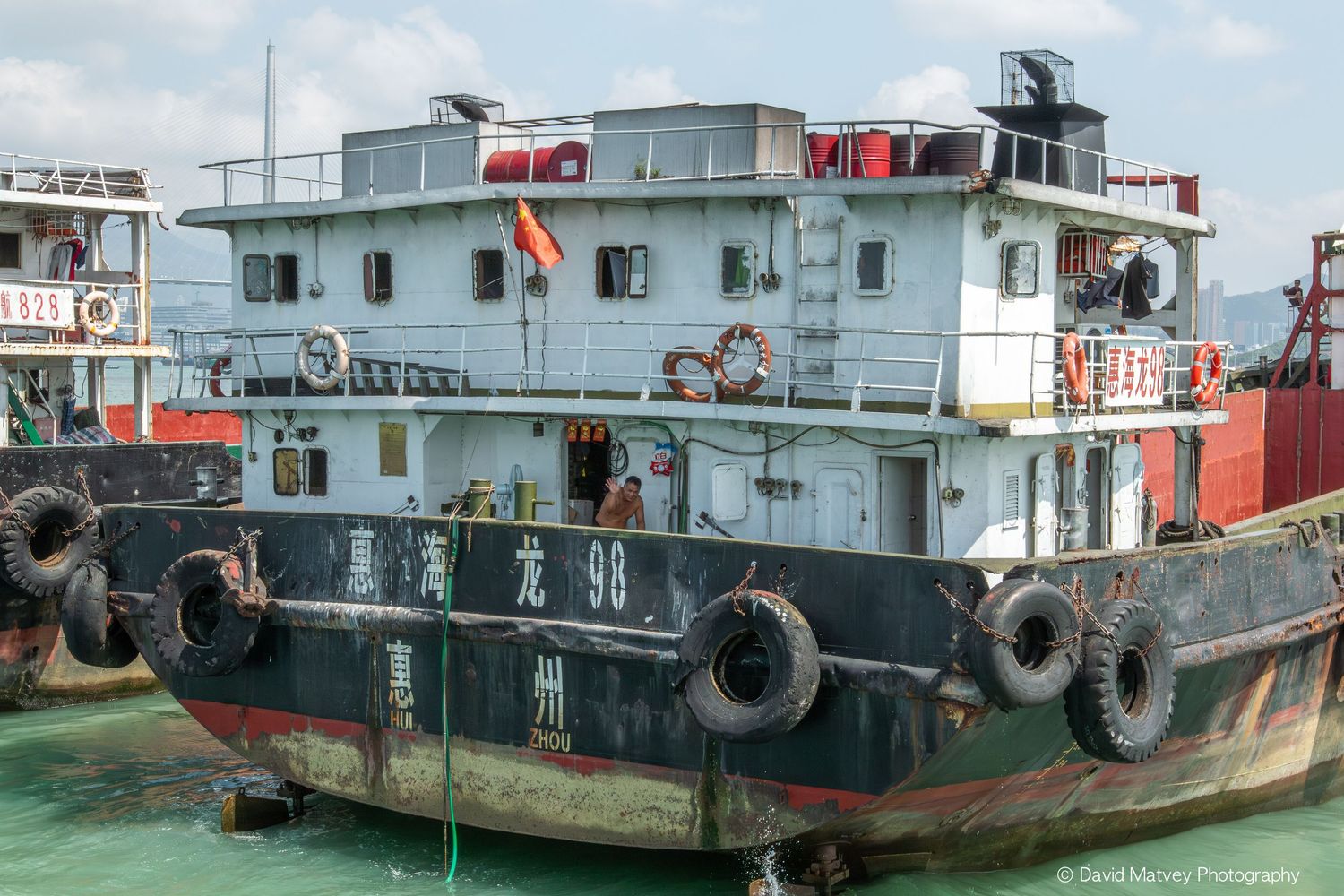 Weathered blue tugboat numbered 98 with Chinese characters docked at a harbor with tires as bumpers.