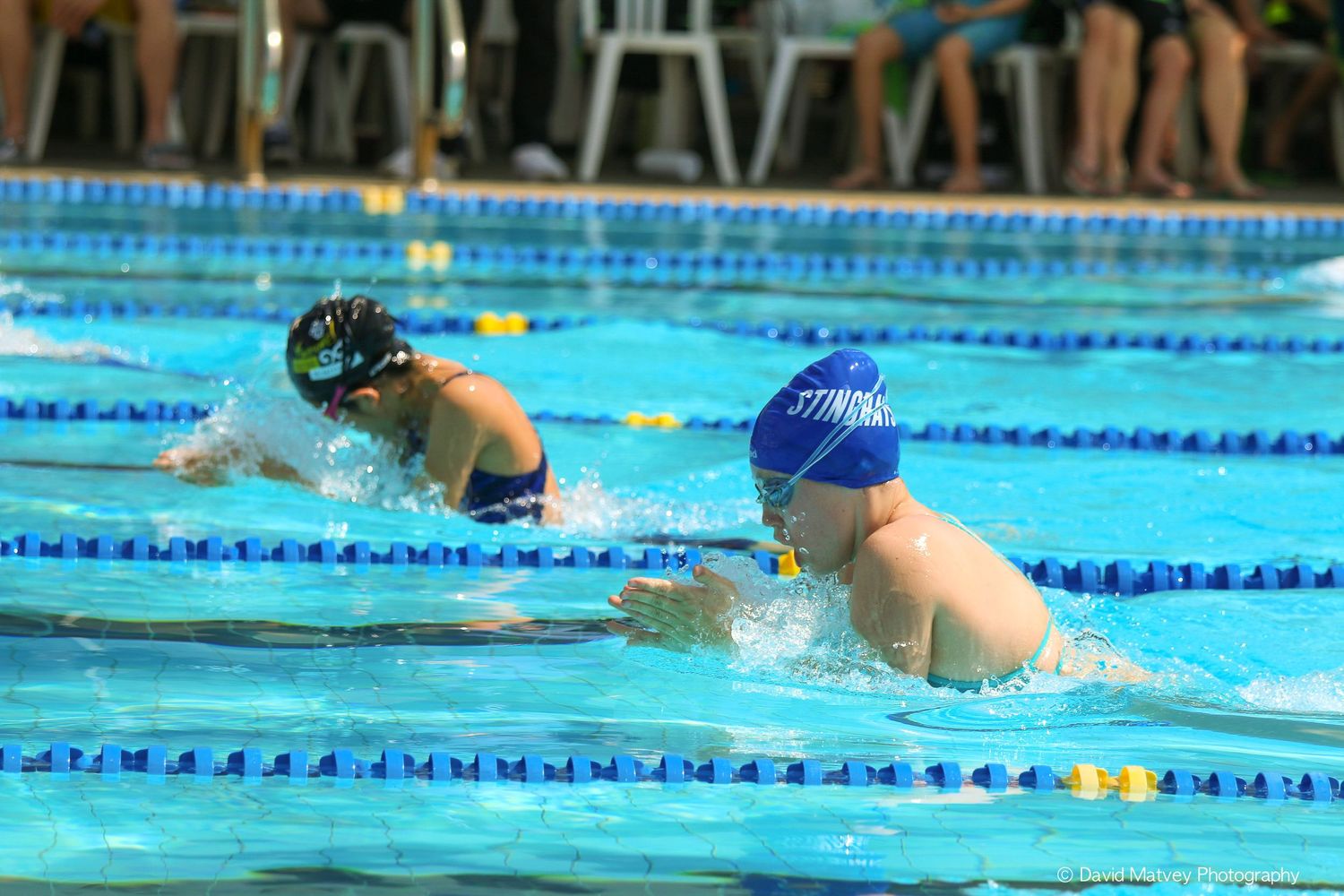 Young swimmers competing in a breaststroke race in an outdoor swimming pool.