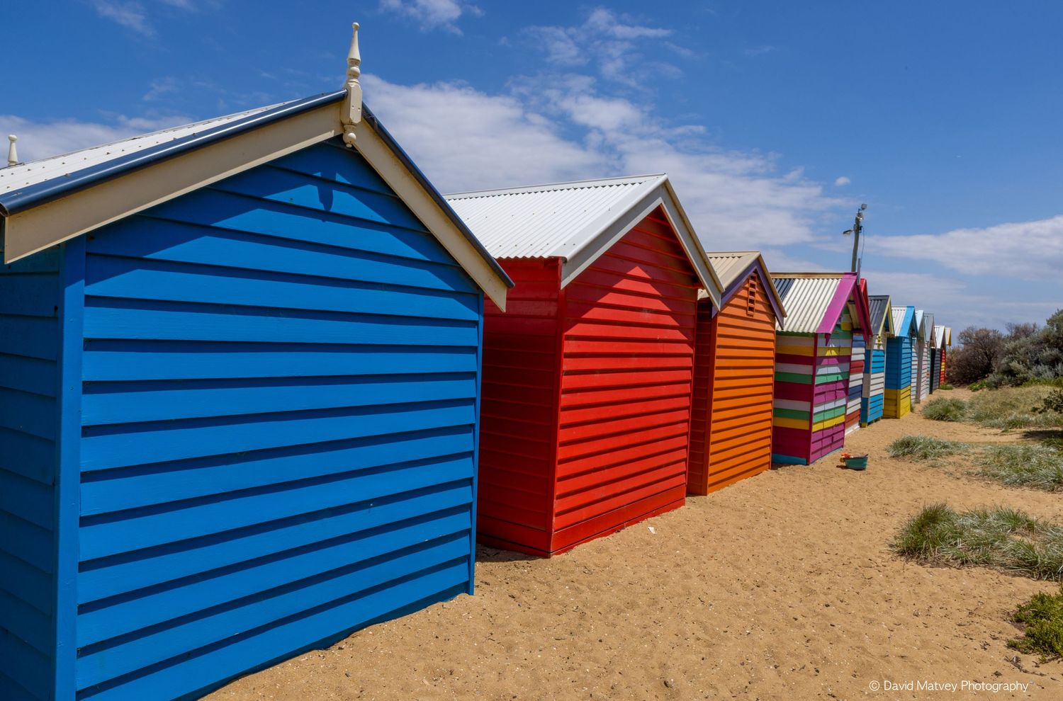 Colorful row of bright beach huts on sandy Brighton beach.
