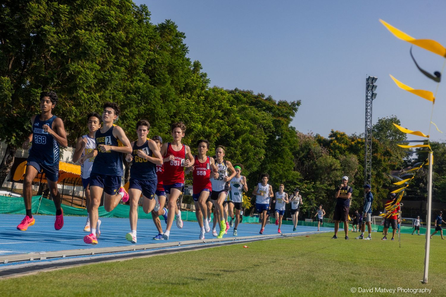 Athletes competing in a track race on a blue running track surrounded by trees.