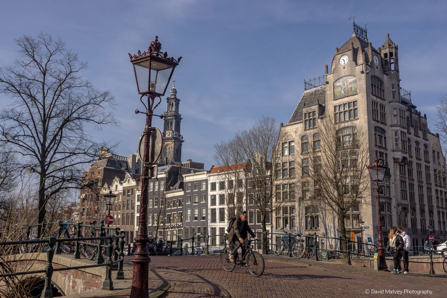 Cyclist crossing bridge in Amsterdam with historic buildings and clock tower.