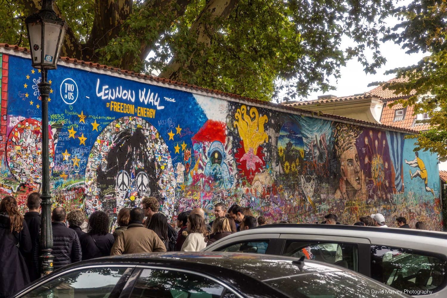Tourists gathered in front of the colorful John Lennon Wall covered in graffiti art in Prague.