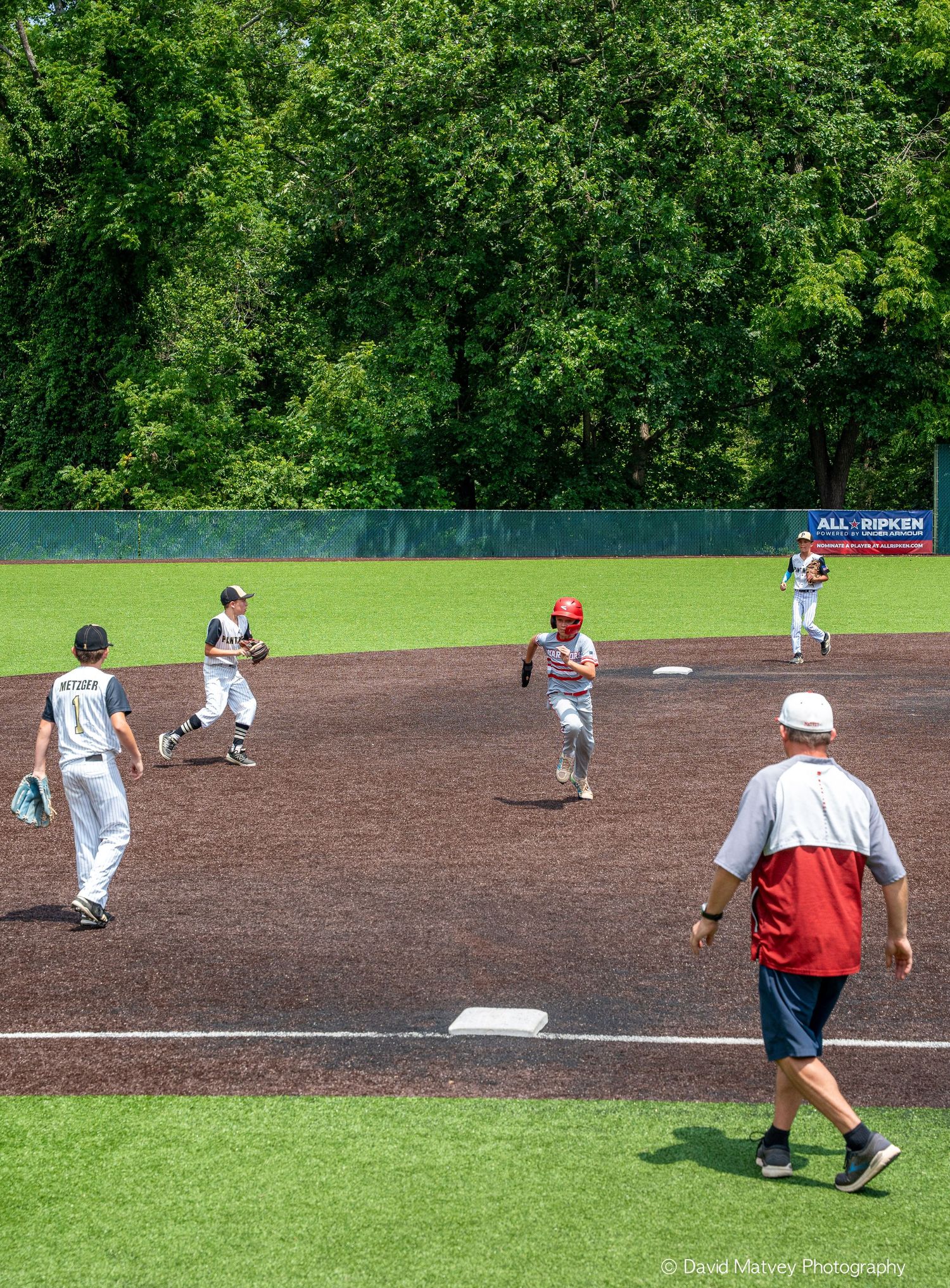 Youth baseball players running bases during sunny outdoor game with coach on field.