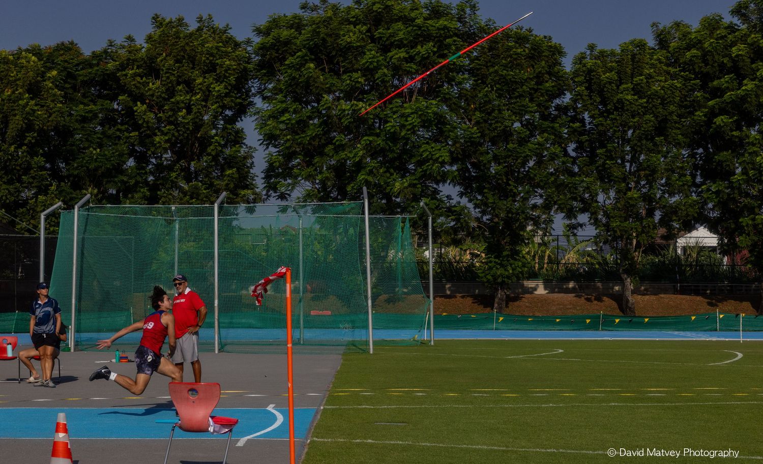 Athlete launches javelin throw on outdoor blue track during field competition.
