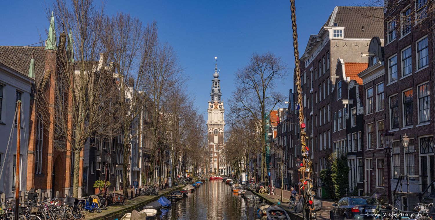 Scenic Amsterdam canal view with historic buildings and Zuiderkerk church tower on a clear winter day.