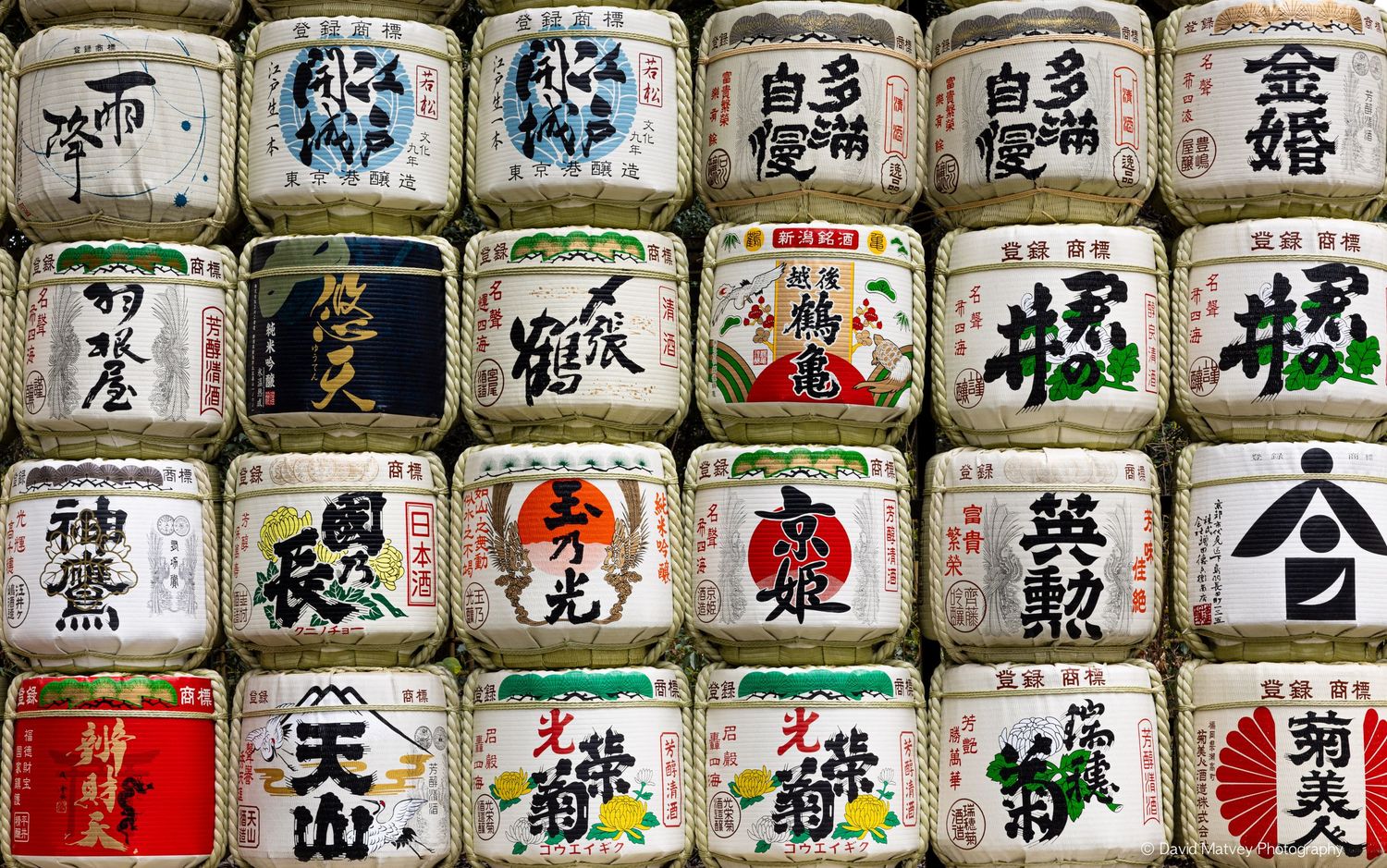 Grid of traditional Japanese sake barrels with colorful kanji labels.