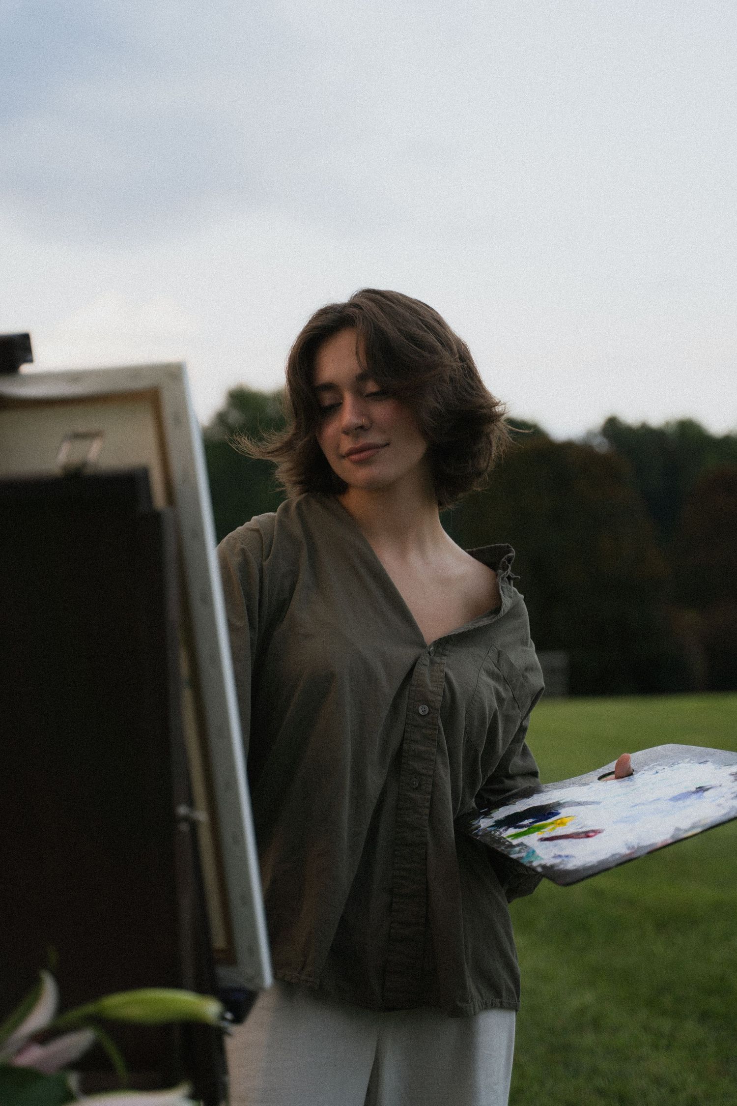 a young woman holds a painter's pallet and looks intently at her canvas on her easel