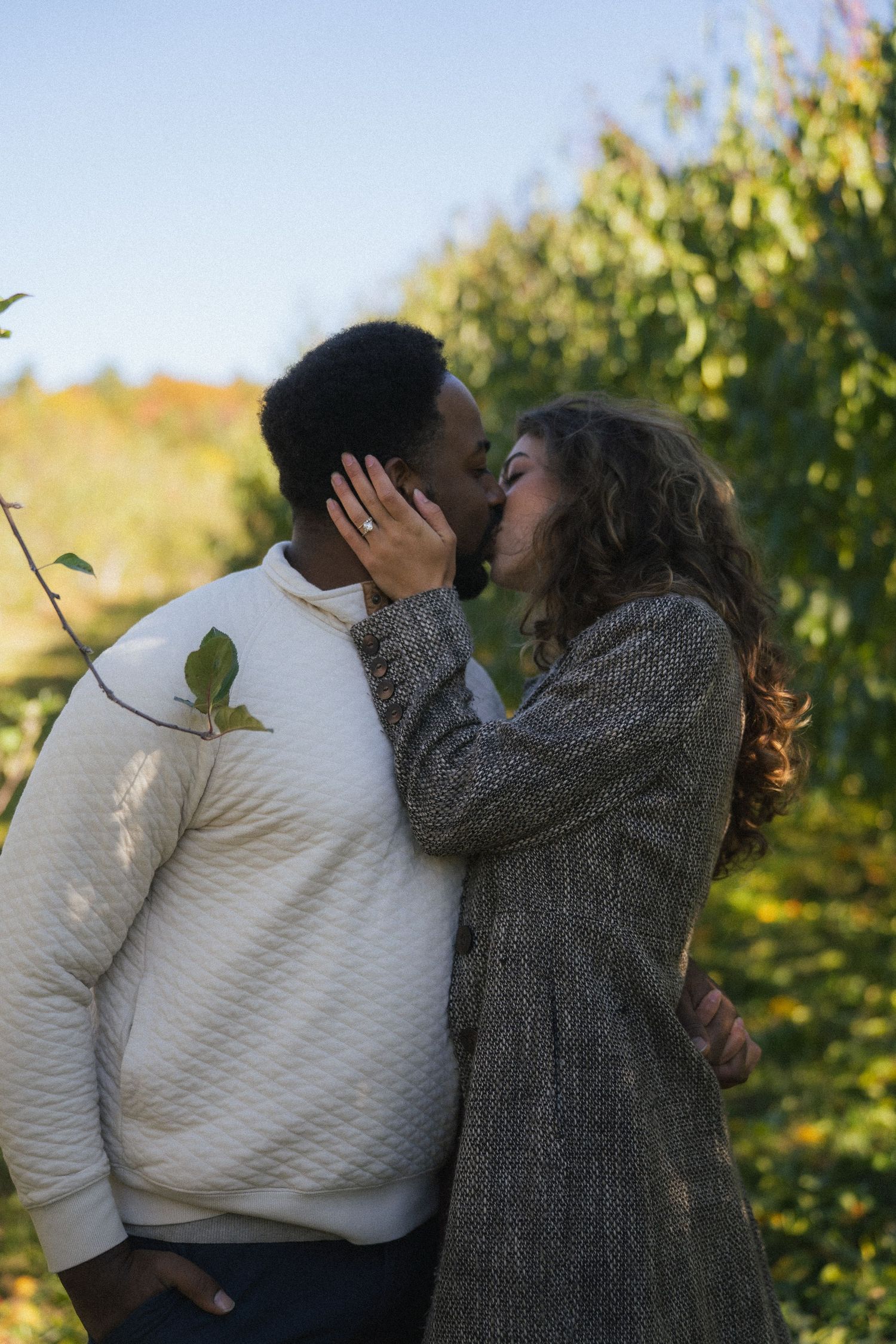 Interracial couple sharing a tender kiss outdoors with colorful autumn foliage in the background.