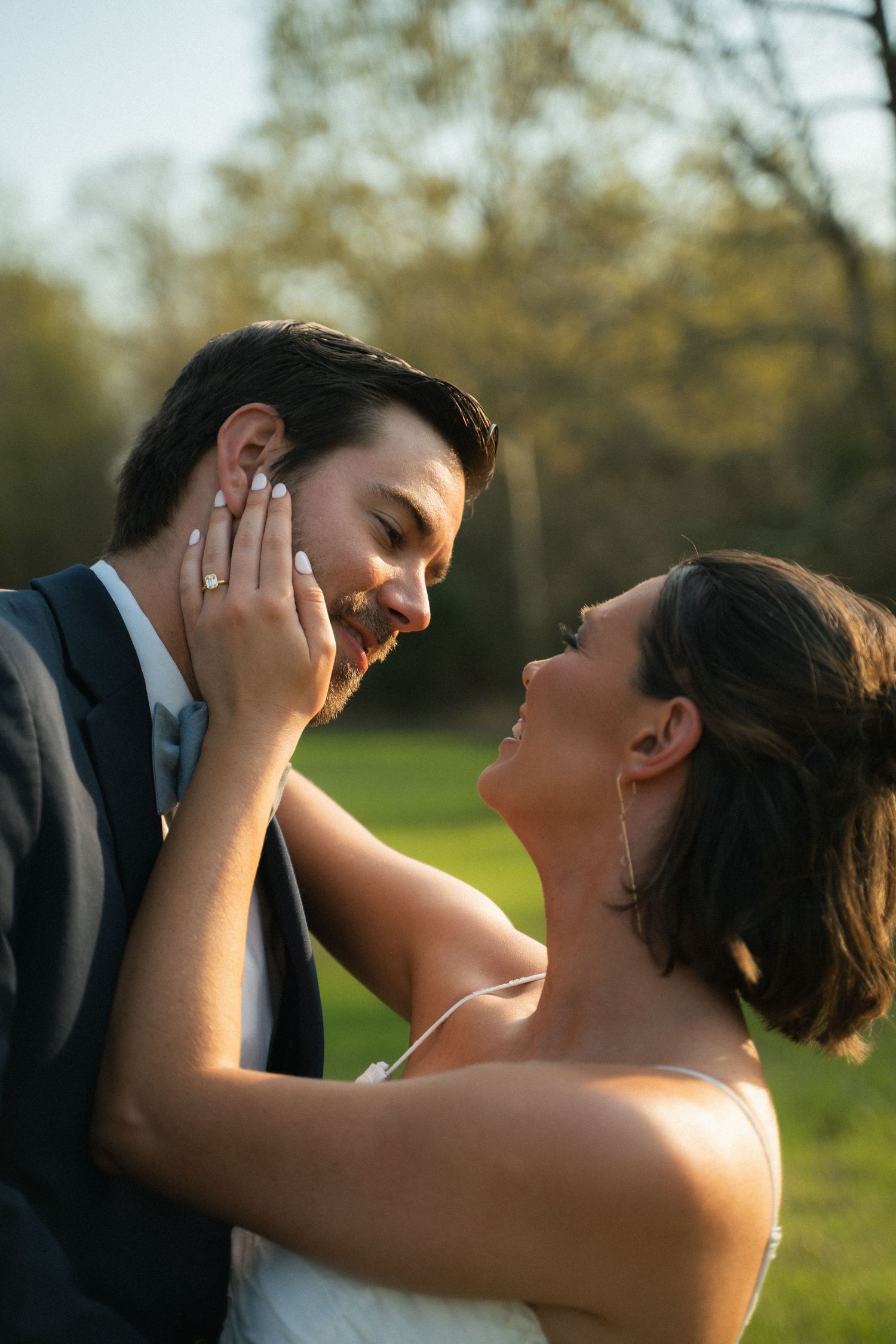 Bride and groom sharing a tender moment outdoors, bride touching groom's face at sunset.