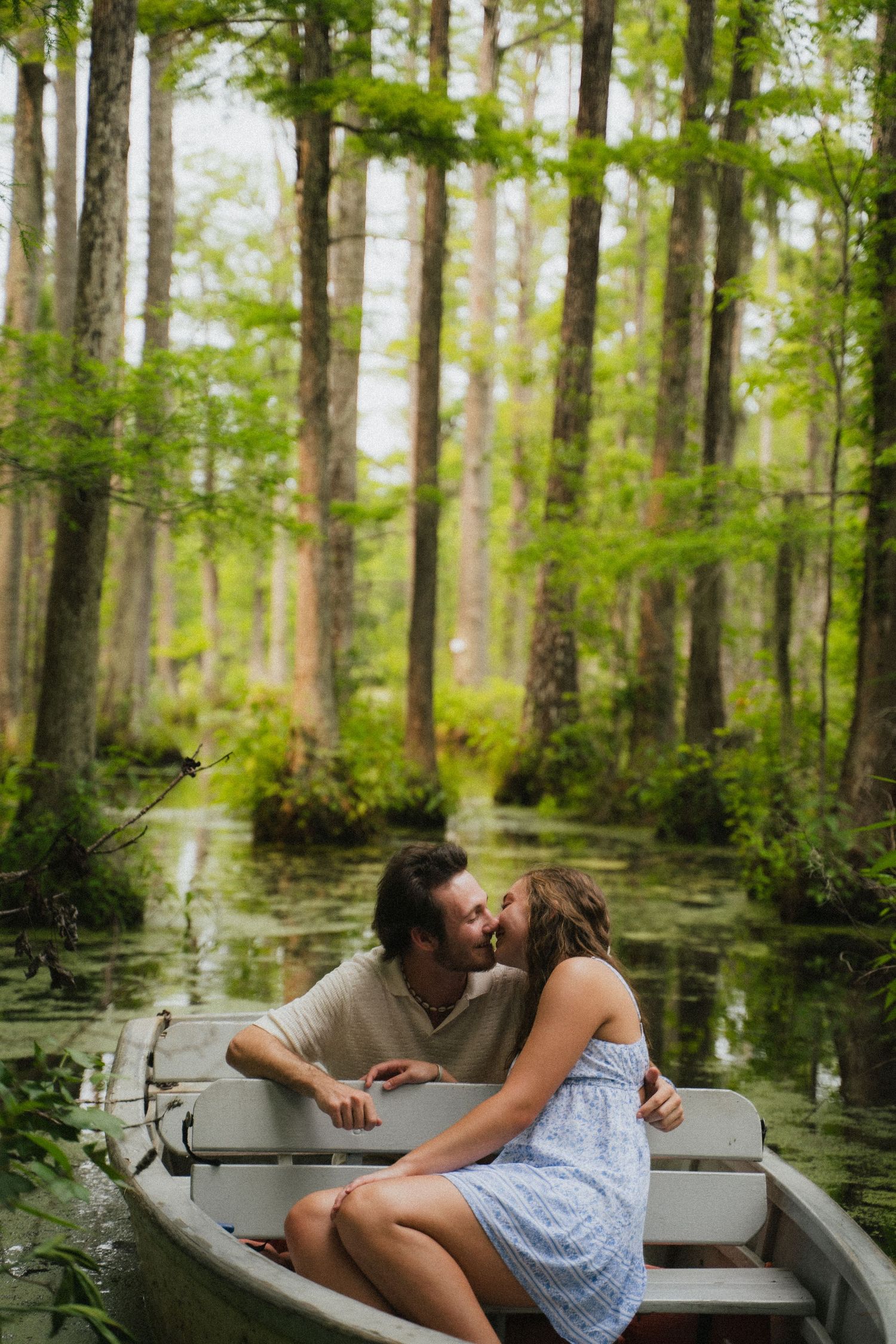 Couple shares a romantic kiss while sitting in a rowboat surrounded by a lush cypress swamp.