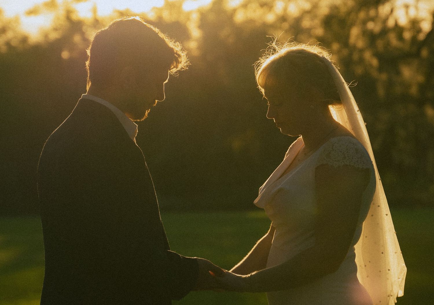 Bride and groom silhouetted against golden sunset light, holding hands in a romantic outdoor wedding portrait.