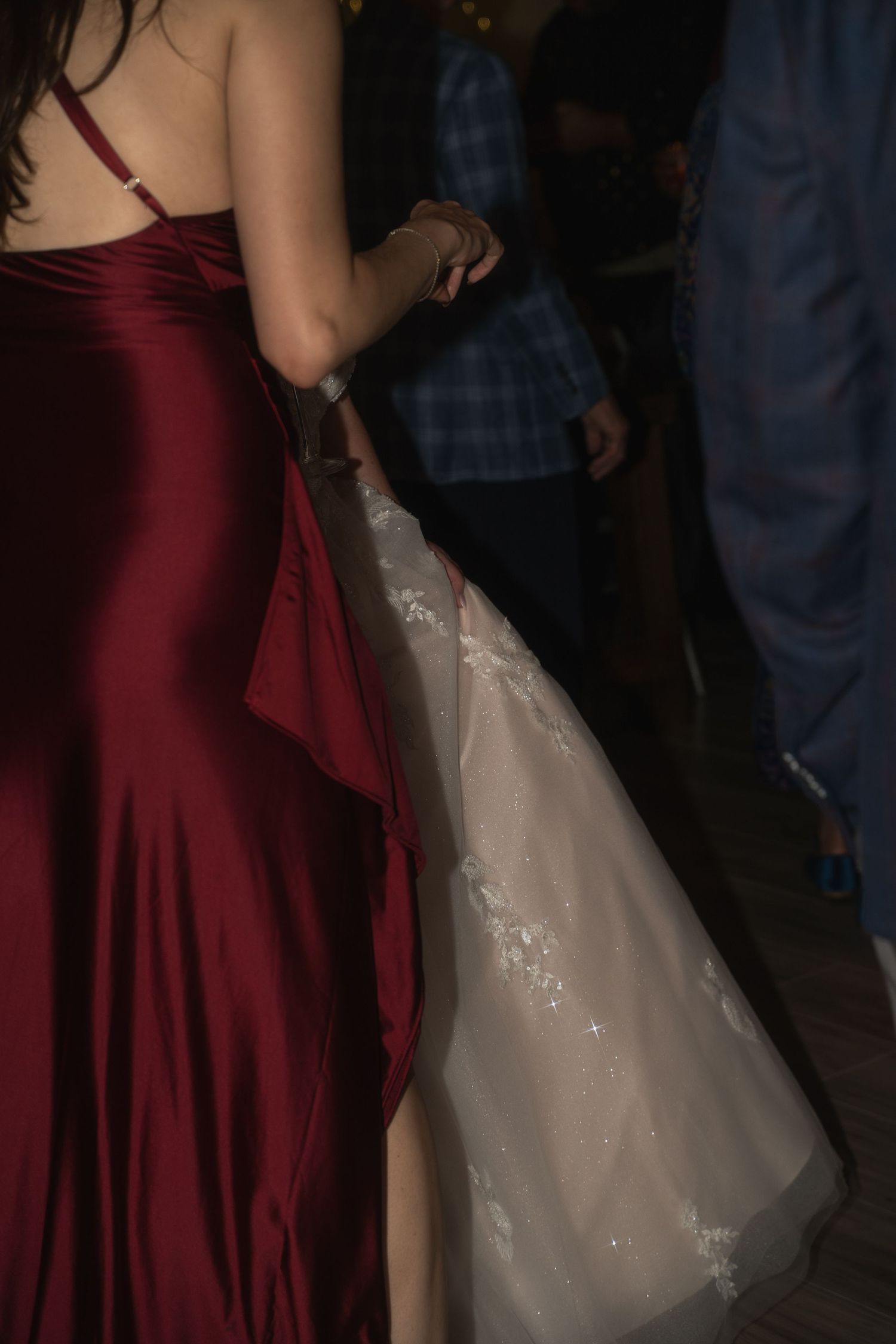 Bride in white lace gown dancing beside bridesmaid in elegant red satin dress.
