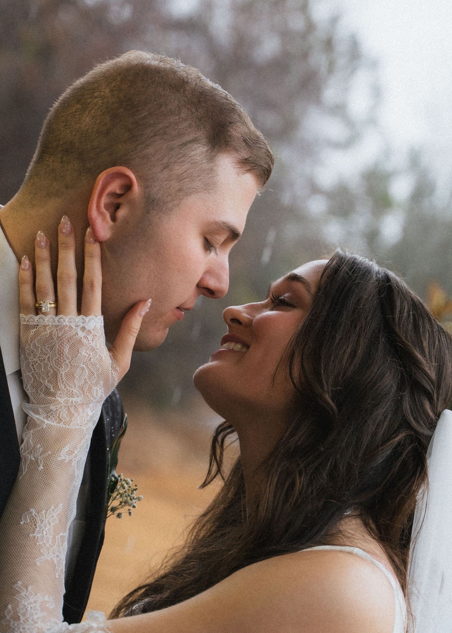 Bride in lace gloves gazes lovingly at groom in intimate rainy outdoor wedding portrait.