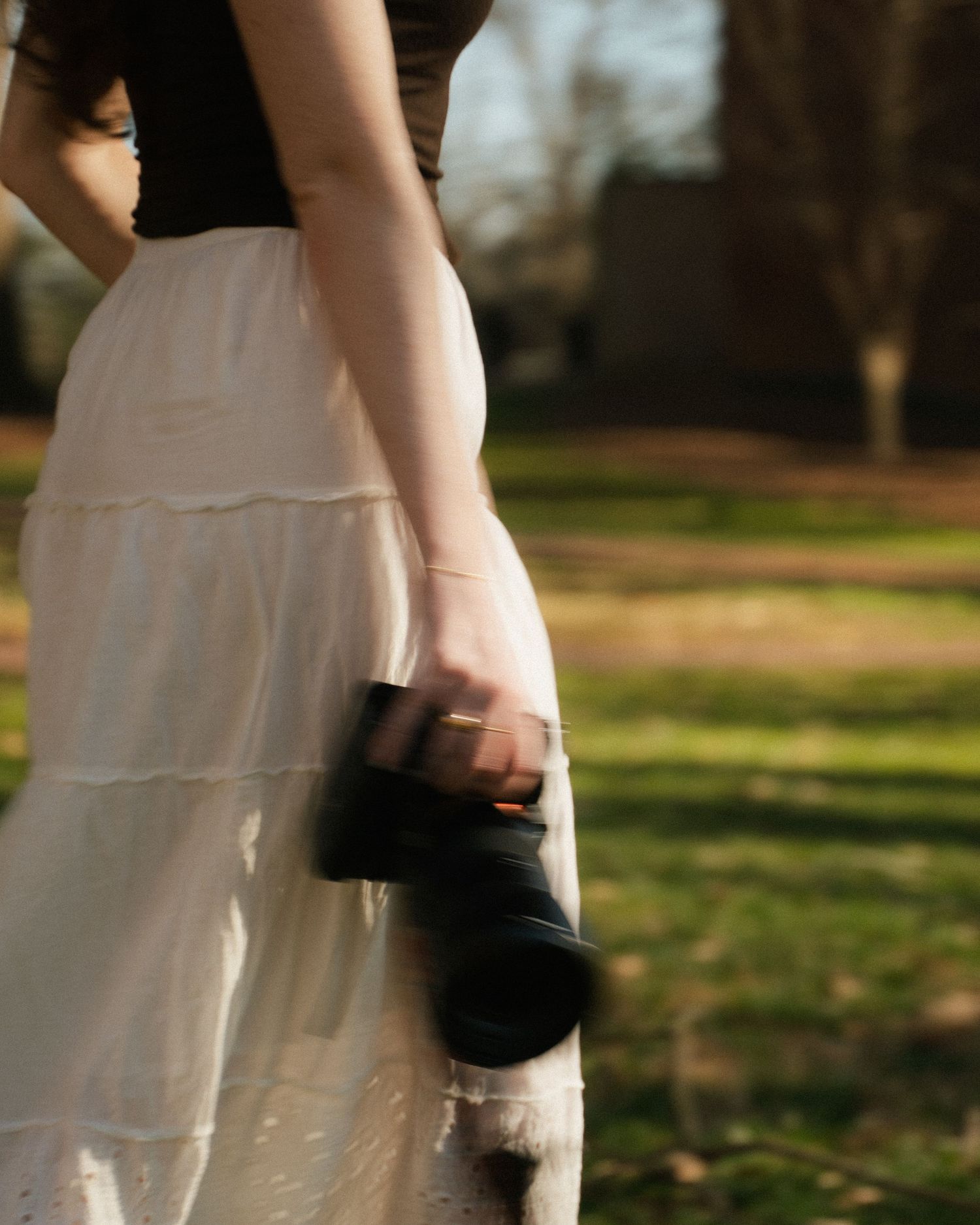 Photographer holding a DSLR camera wearing a white skirt outdoors in sunlight.