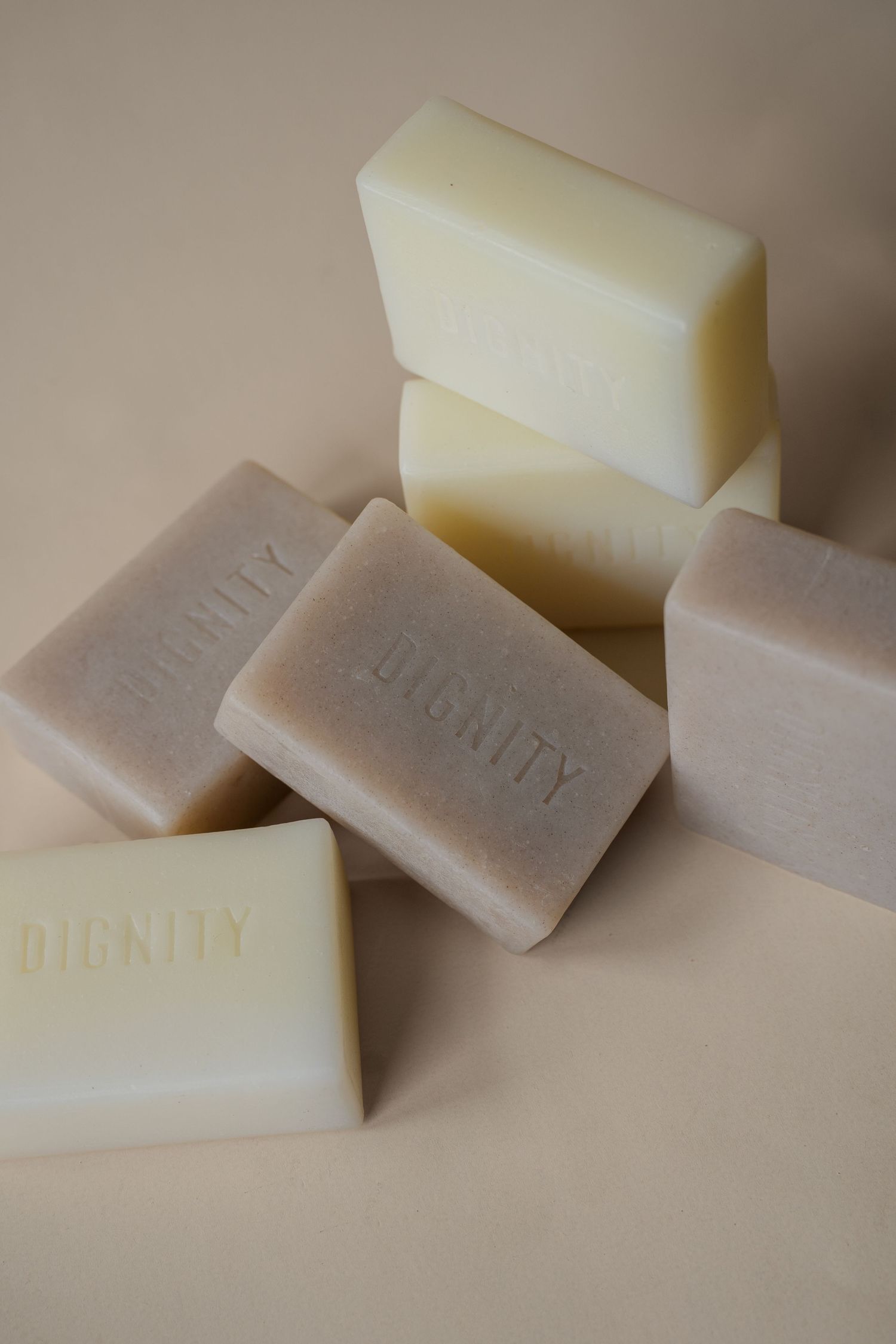 Six bars of Dignity branded soap in cream and beige tones arranged on a neutral background.