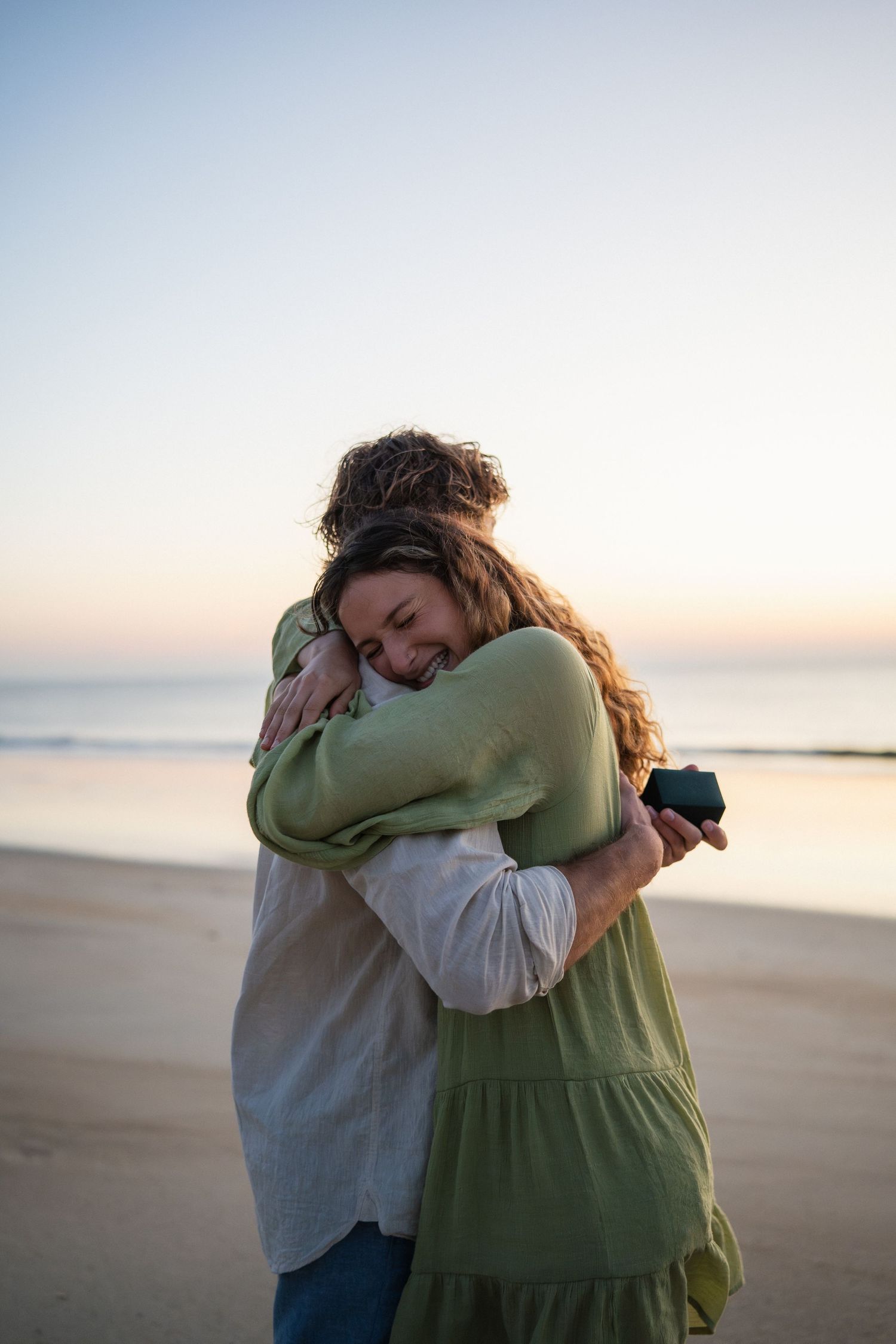 Happy couple embracing on beach at sunset with colorful sky in background.