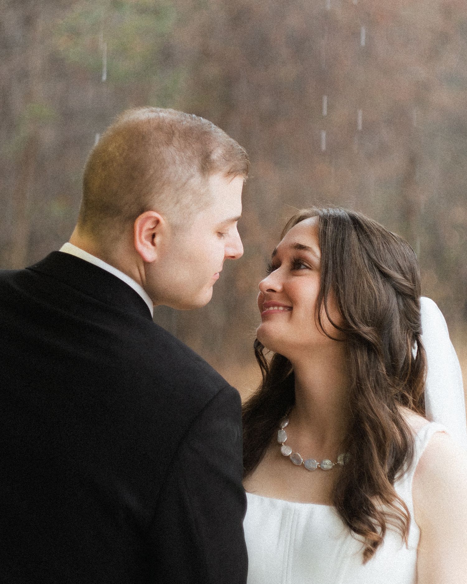 Bride smiling at groom in the rain during intimate outdoor wedding portrait session.