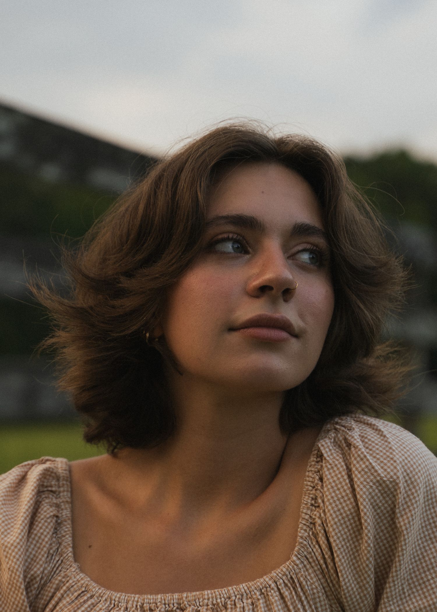 Young brunette woman with short wavy hair gazing upward outdoors in a vintage-style square-neck blouse.