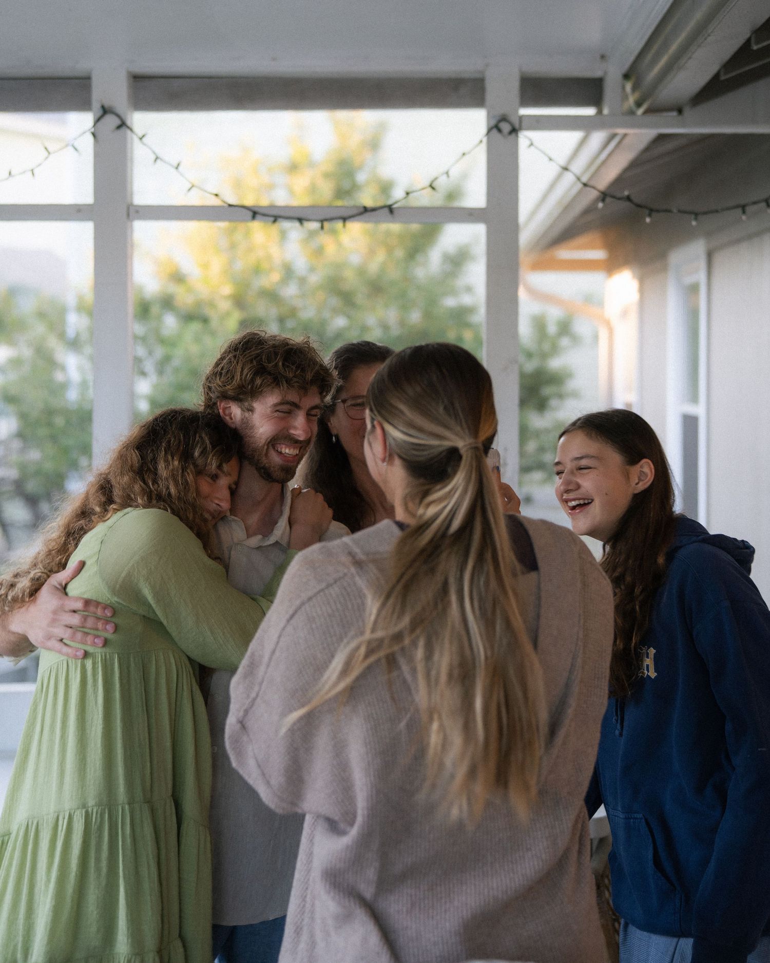 Group of happy friends sharing a warm hug and laughing together on a decorated porch.