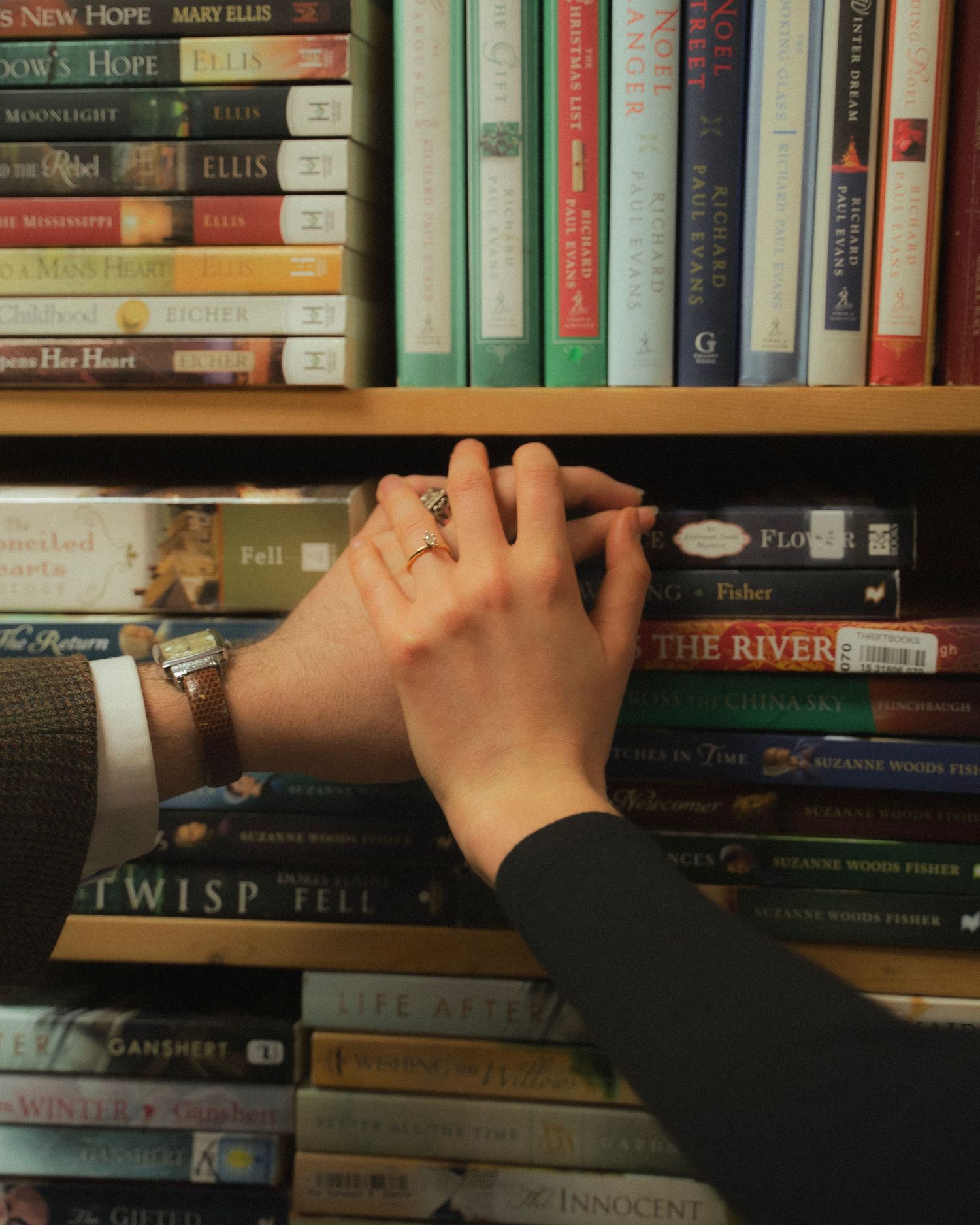 Two hands holding over a colorful bookshelf filled with novels in a cozy library setting.