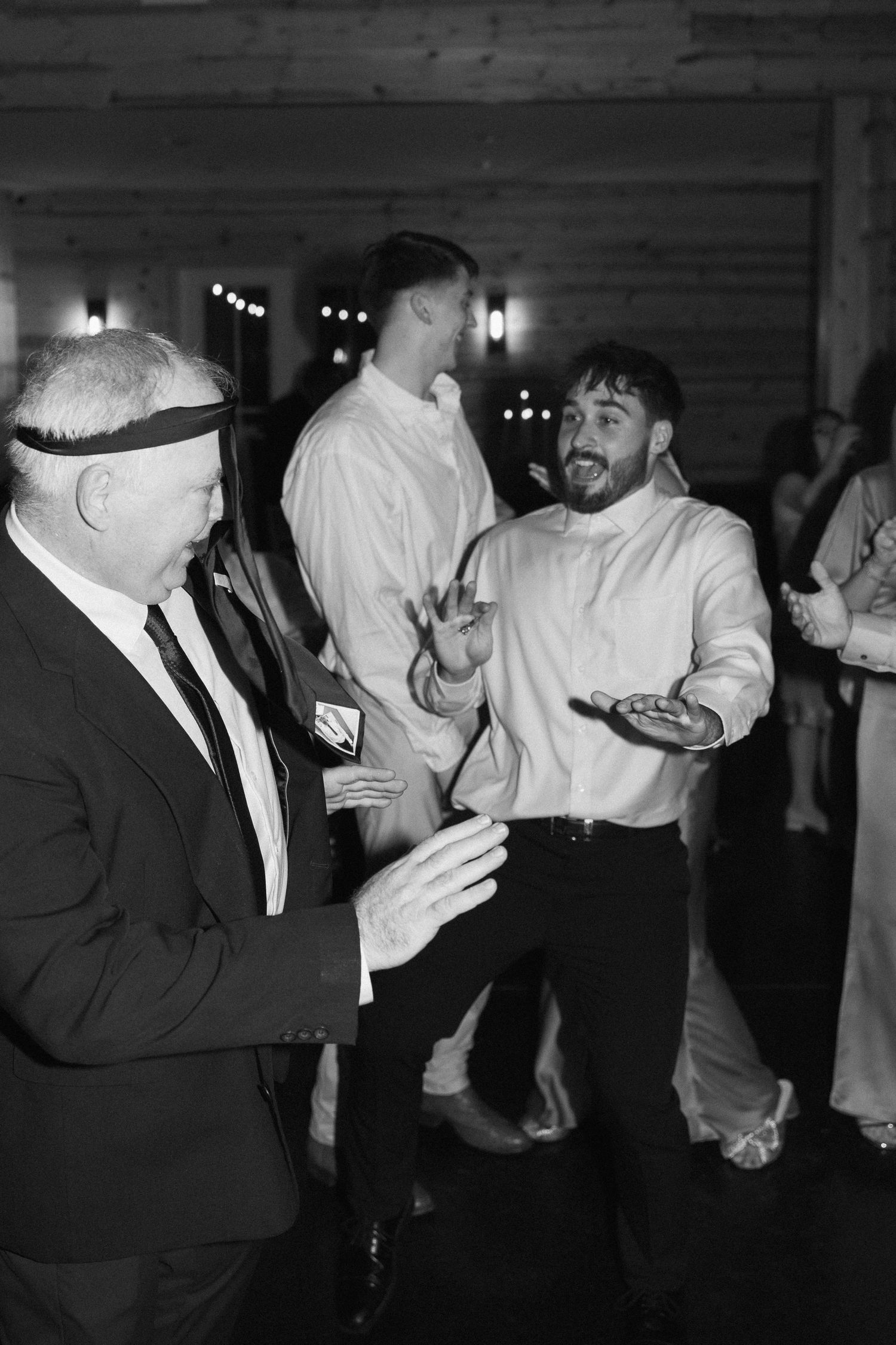 Black and white photo of wedding guests dancing and laughing together at an elegant evening reception.