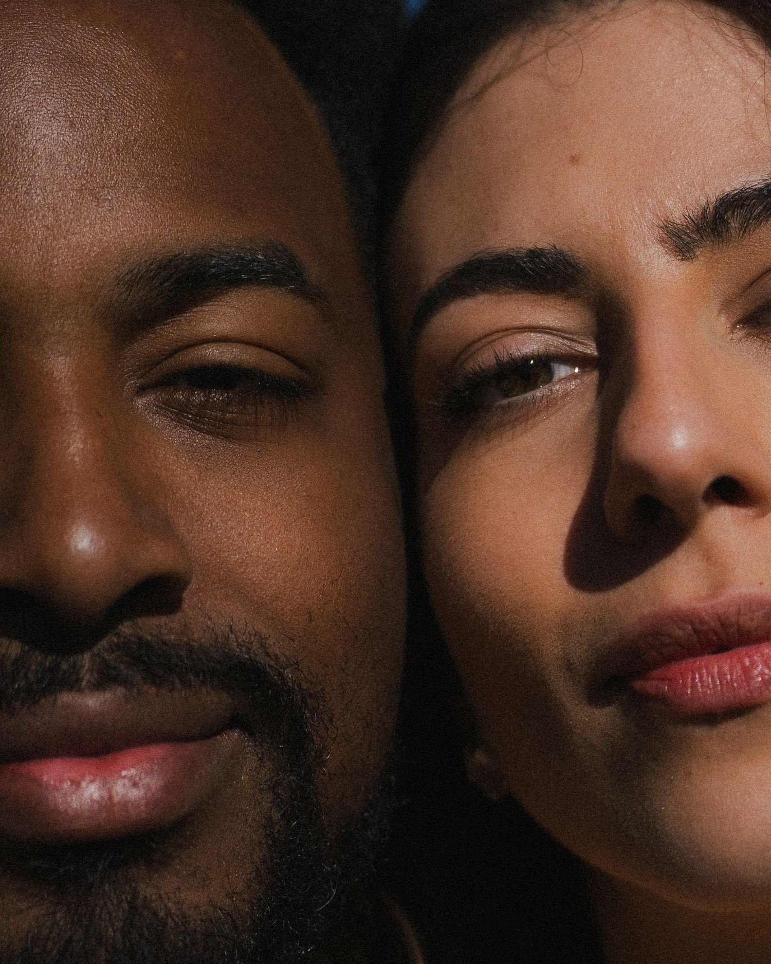 Intimate close-up portrait of interracial couple with faces together in dramatic lighting.