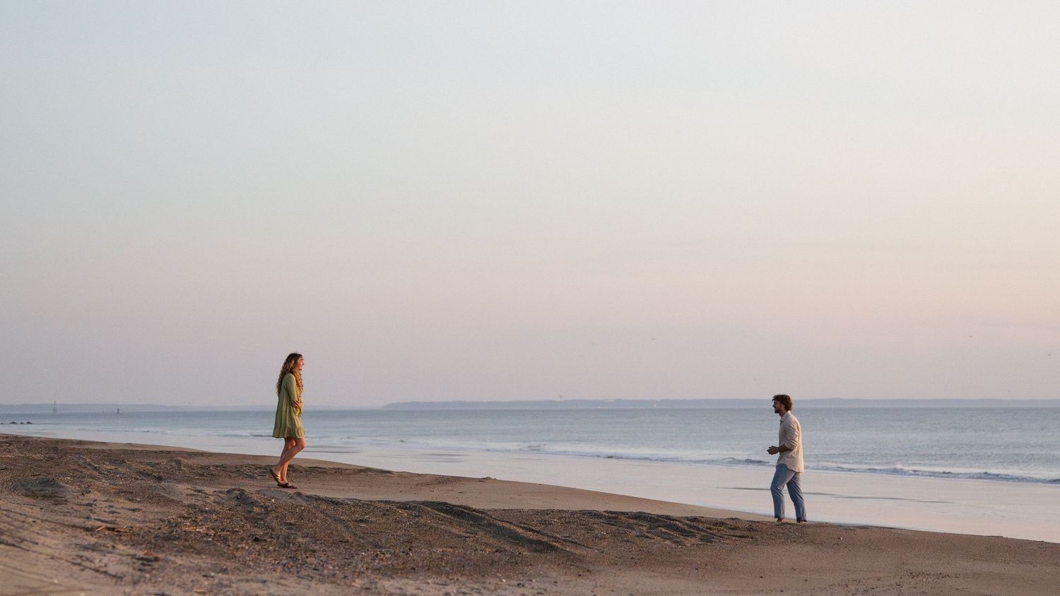 Two people strolling along a quiet beach shore at twilight with soft pastel horizon colors.