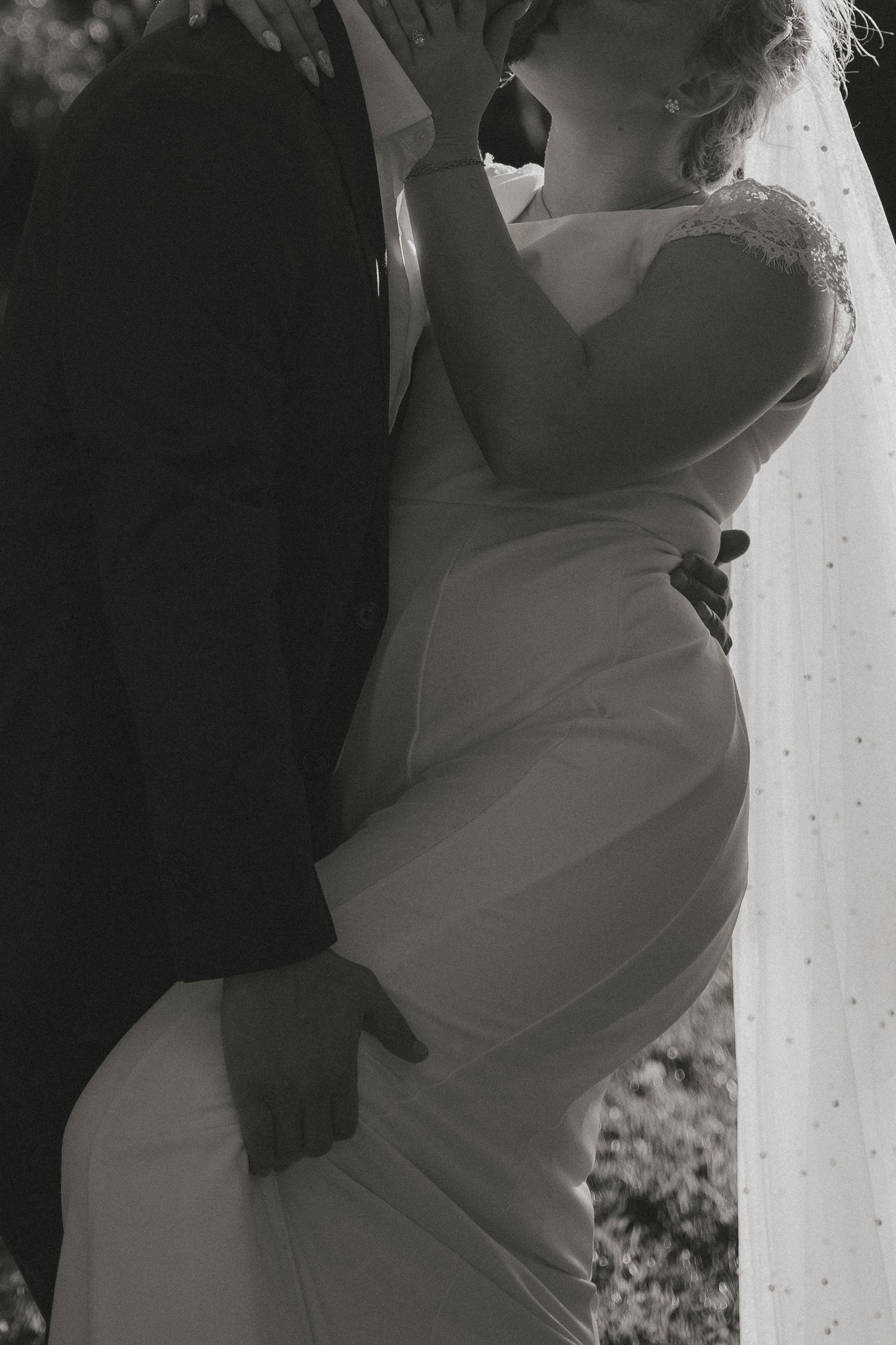 Black and white intimate portrait of bride in lace gown embracing groom at wedding celebration.