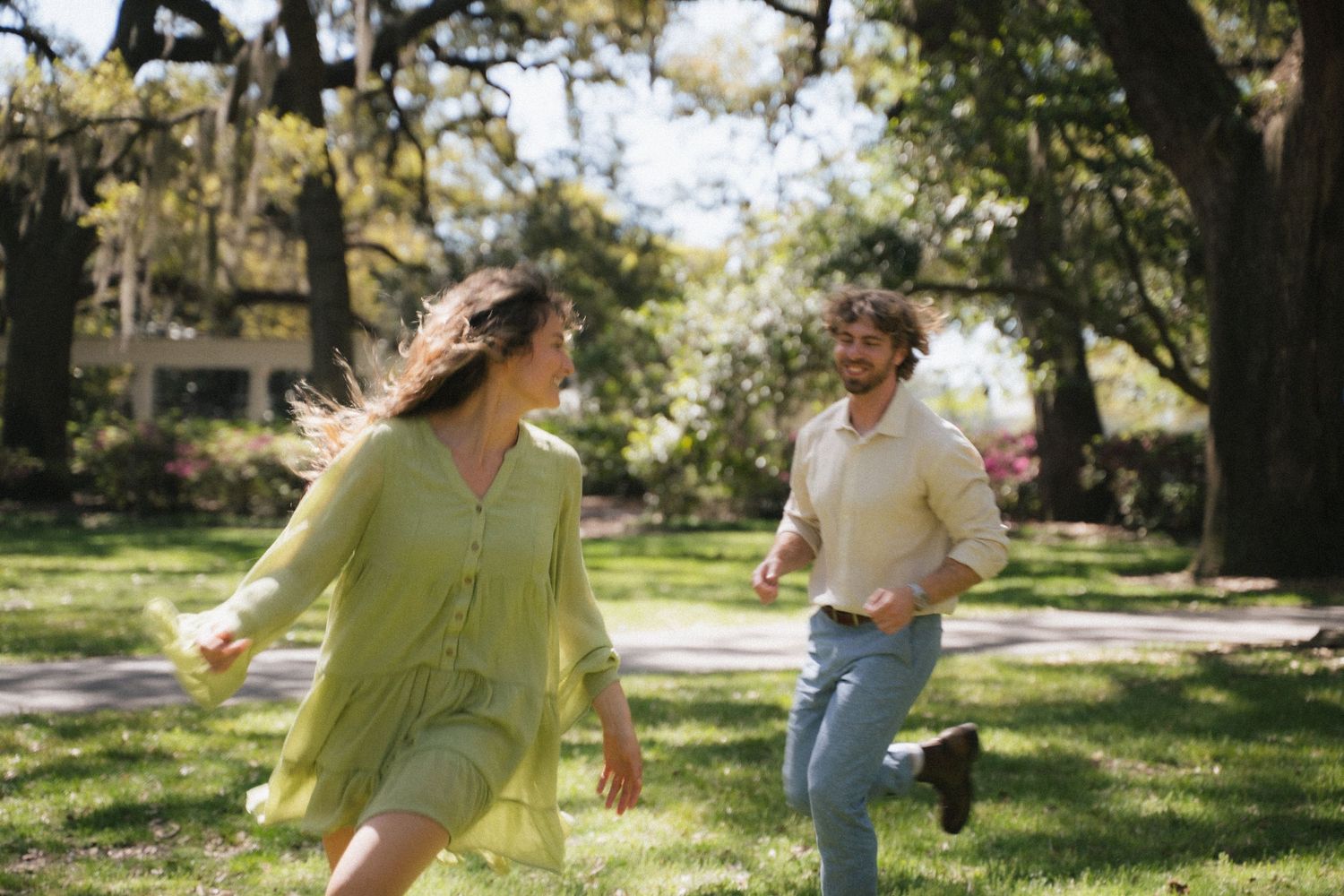 Happy couple runs and laughs together through sunny tree-lined park on bright day.