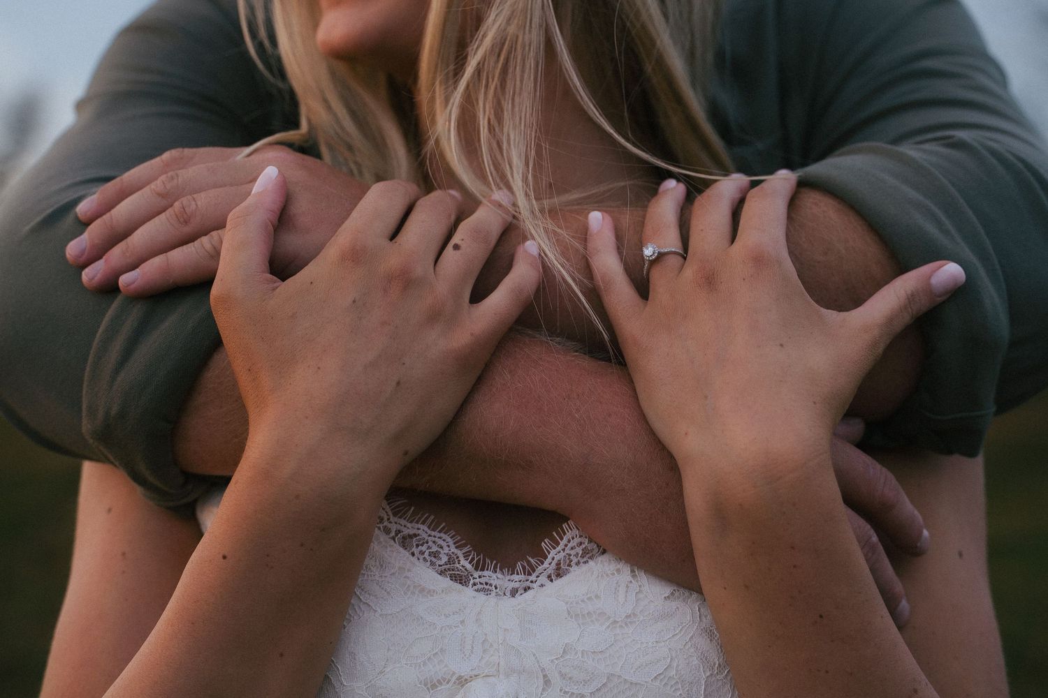 Close-up of a couple embracing, showing a diamond engagement ring on the womans hand.