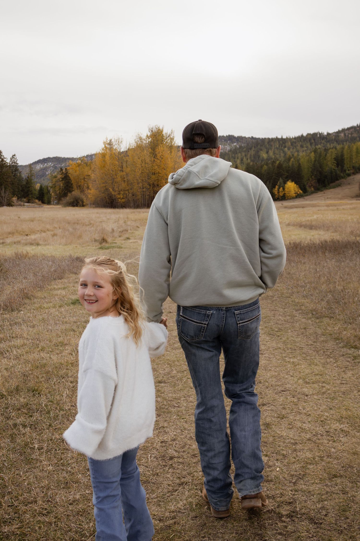 A dad walking holding hands with his daughter during a fall family session in Kalispell Montana