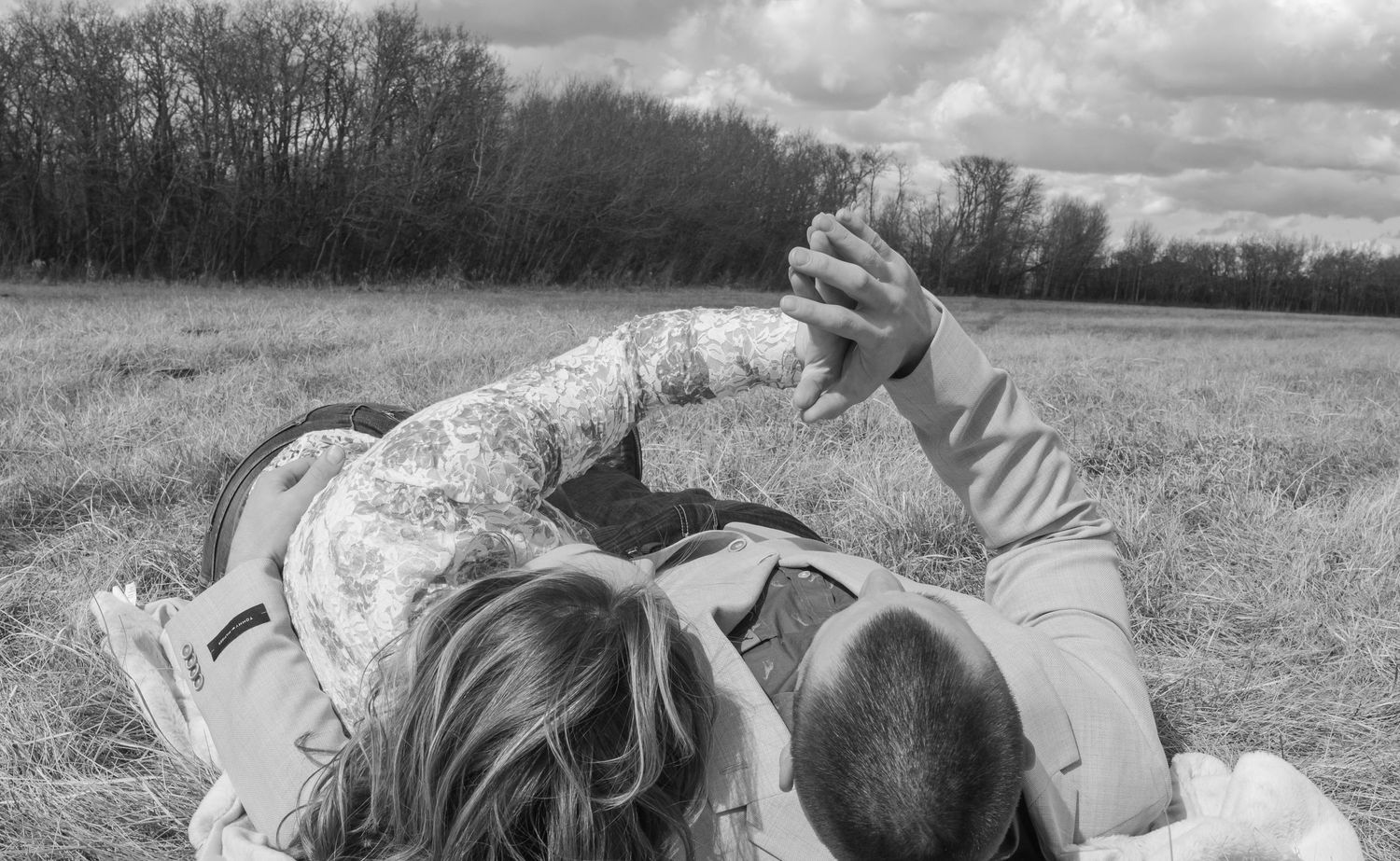 A couple laying in the field together caressing hands during an engagement session in Havre, Mt