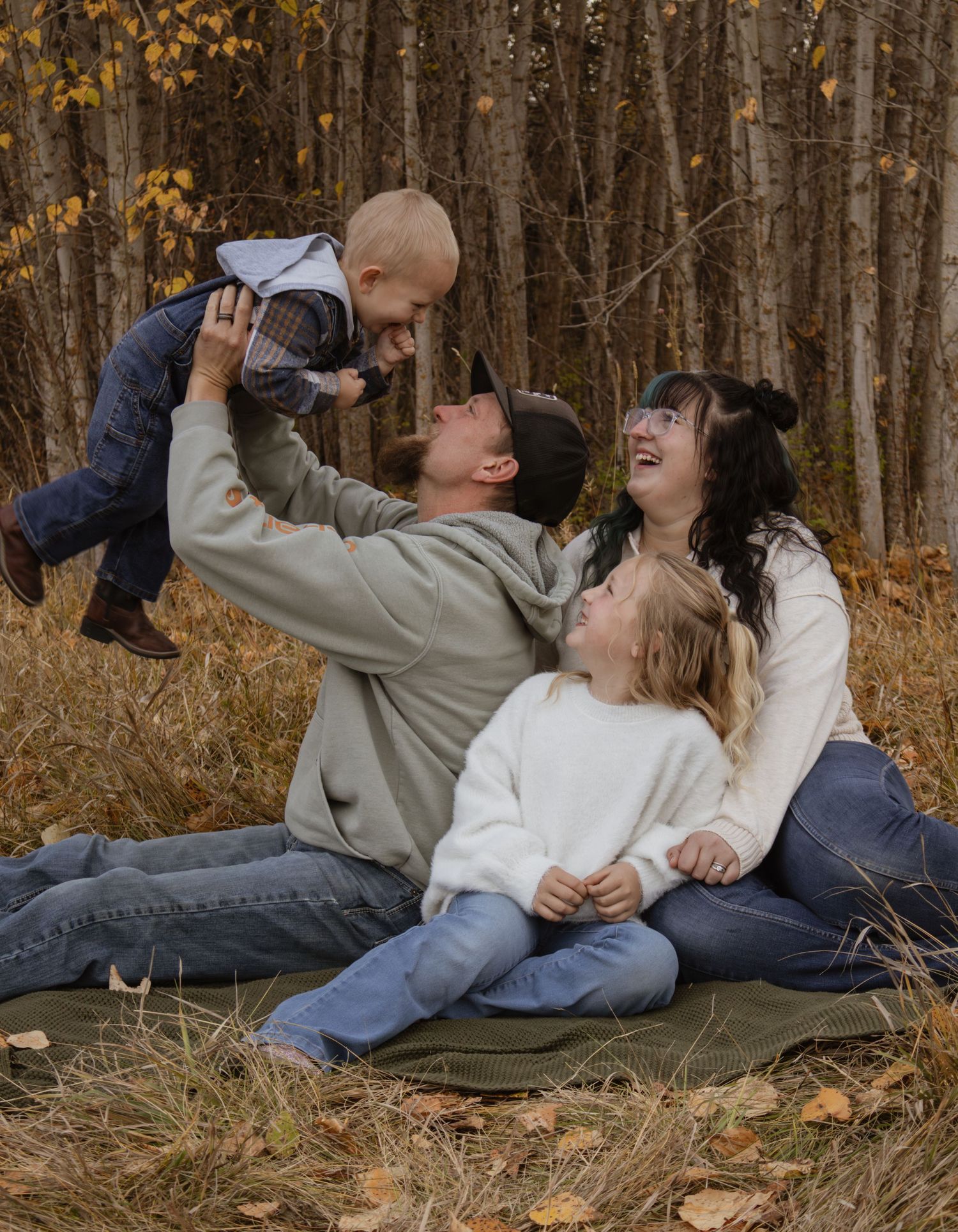 A family of four sitting together while dad lifts up the toddler in the air during a family session in Kalispell Montana