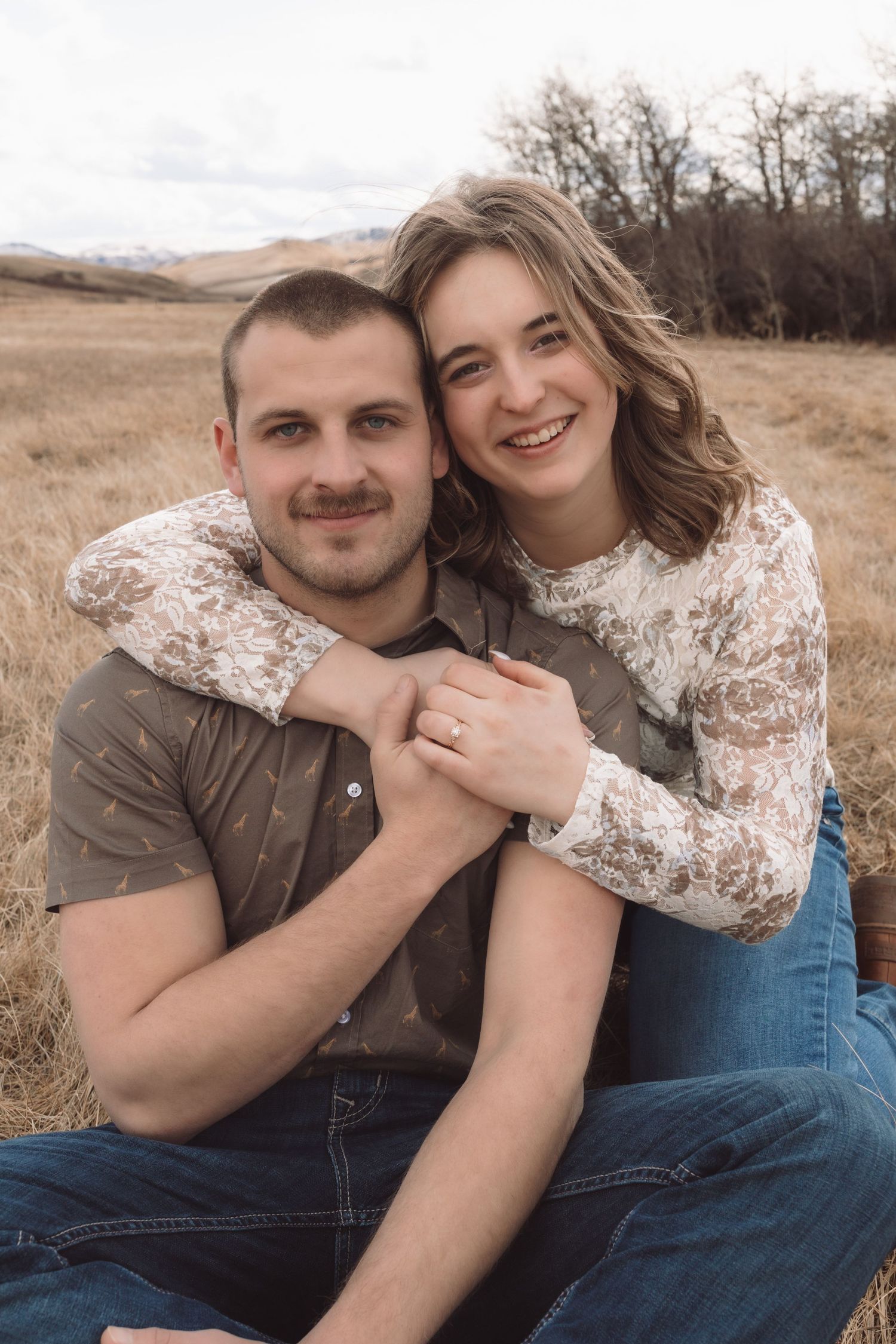 A couple sitting together while the woman wraps her arms around her fiancé during an engagement session in Havre, Mt