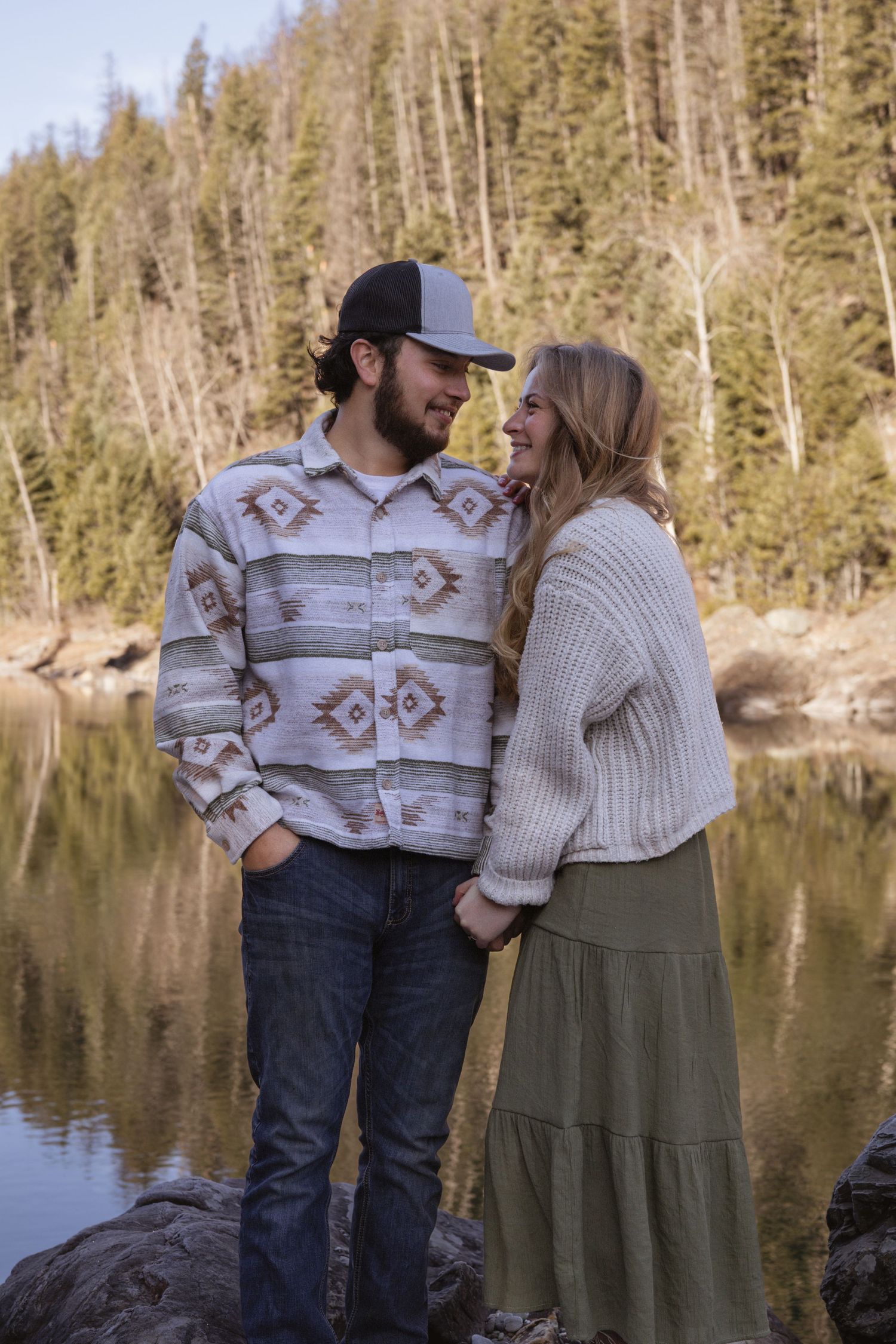 A couple holding hands looking at each other next to a river during a couples session in West Glacier Montana