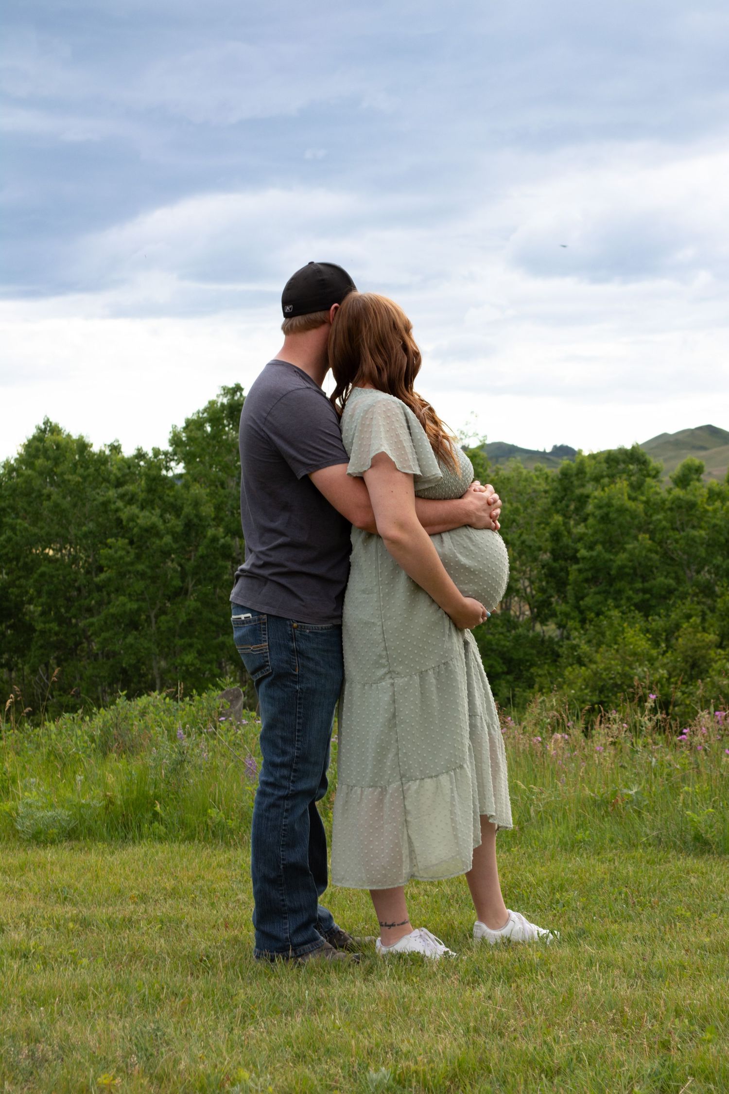 A mother and father holding her expecting baby belly while looking at the view during a maternity session in Havre Montana