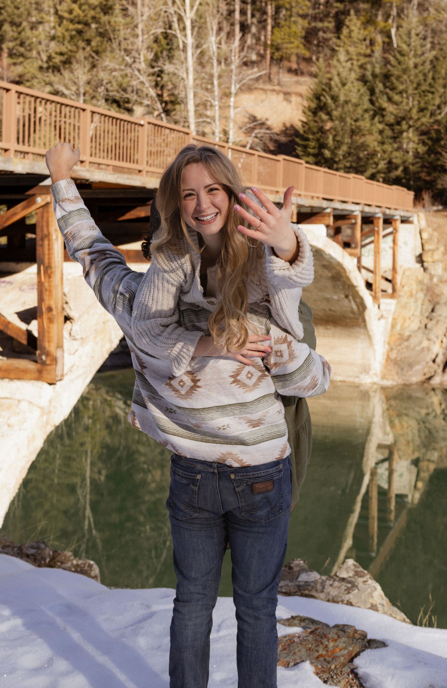A man holding his Fiancé on his shoulder while she shows off her ring during an engagement session in West Glacier Montana
