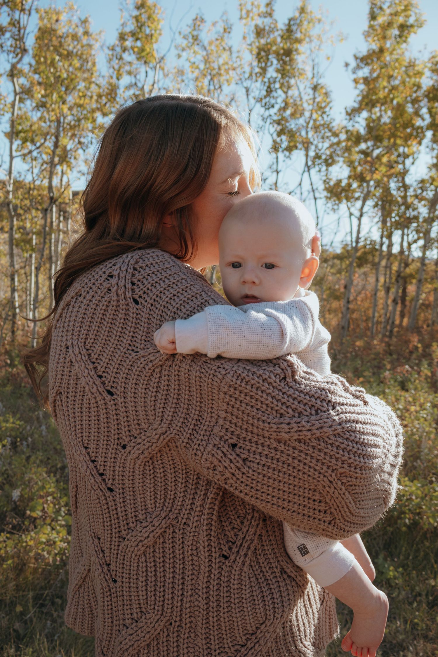 A mother holding her baby close while the sun shines down on them during a mommy and me session in Havre Montana