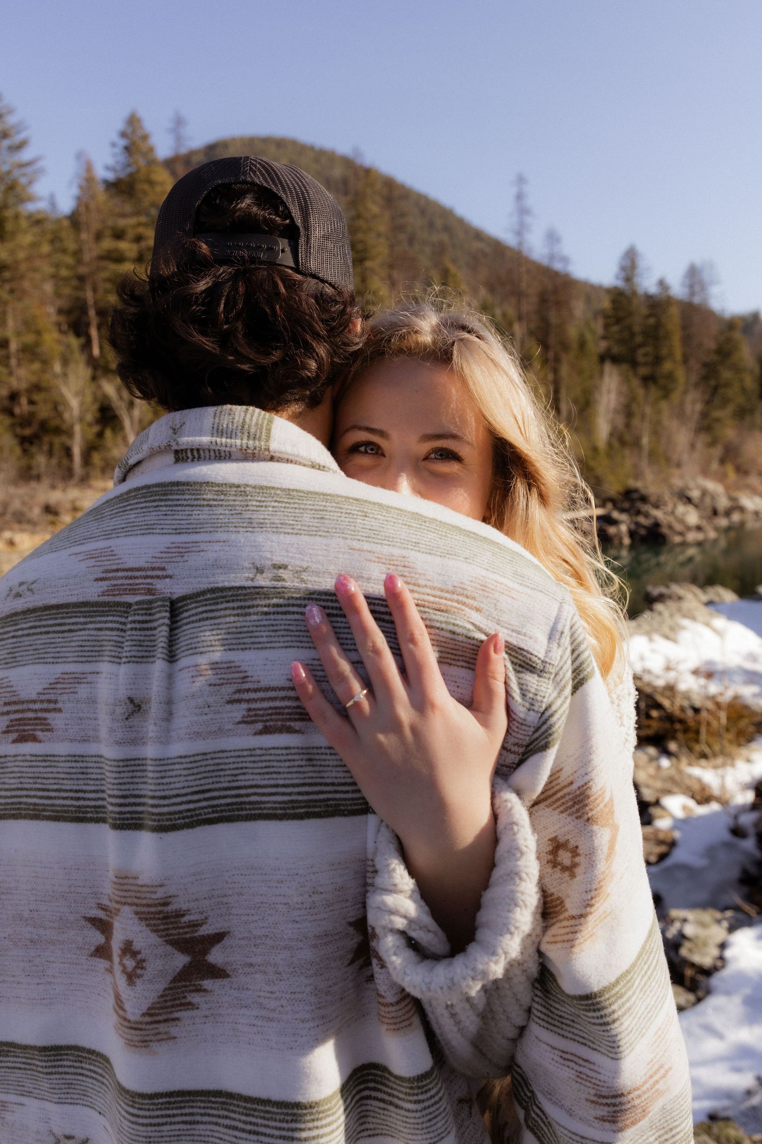A women hugging her fiancé while showing her ring during a couples session in West Glacier Montana
