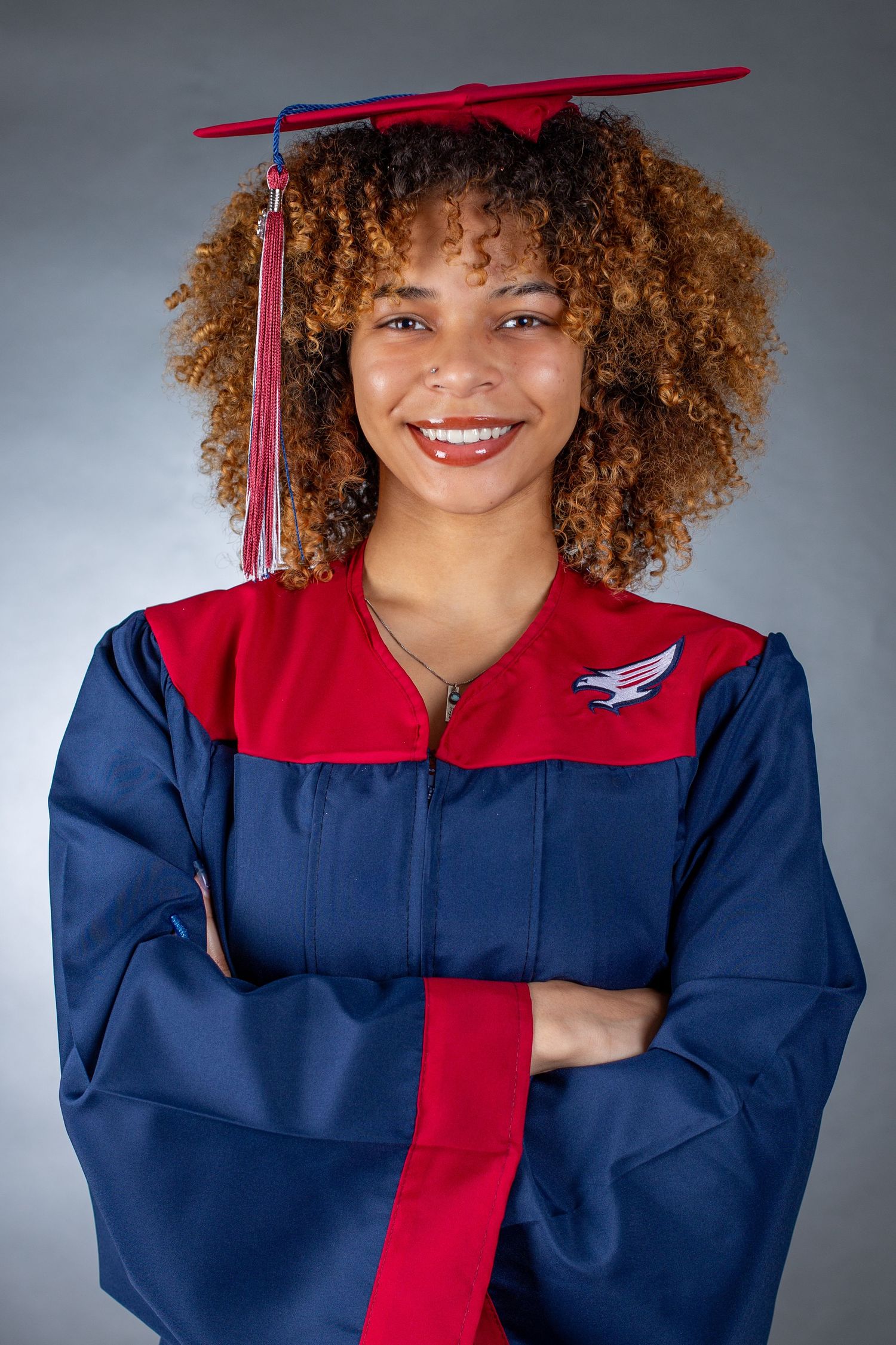 Graduate in navy blue and red academic regalia smiles brightly while posing for graduation photos.