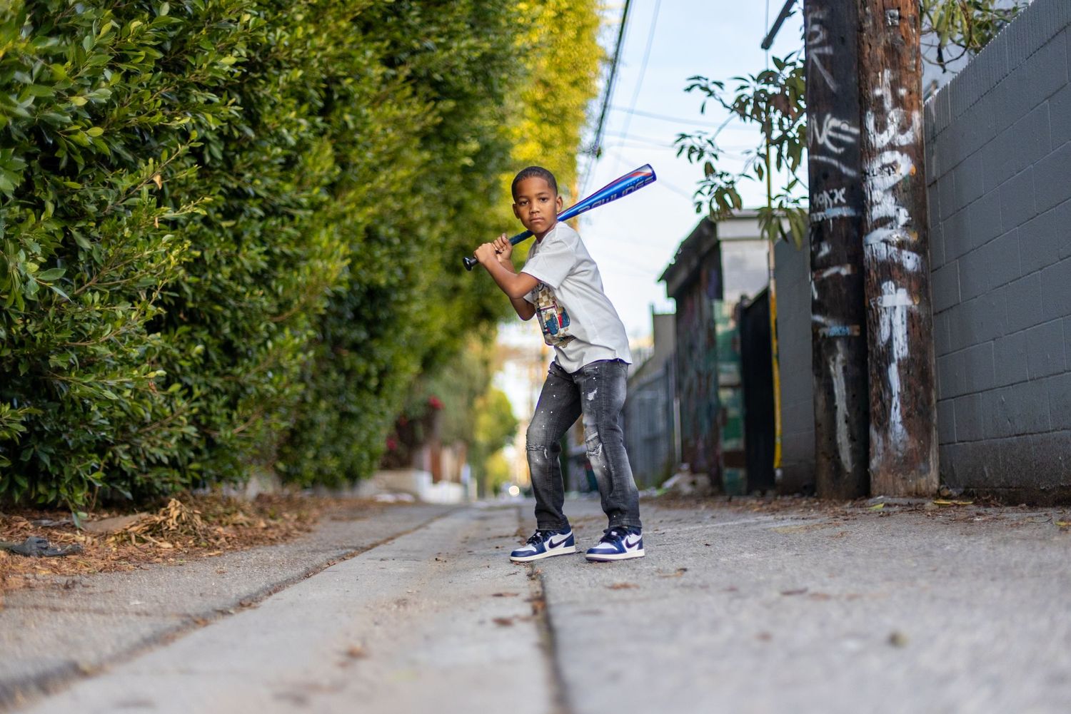 A person in alley while performing a trick with a blue baseball bat in hand.