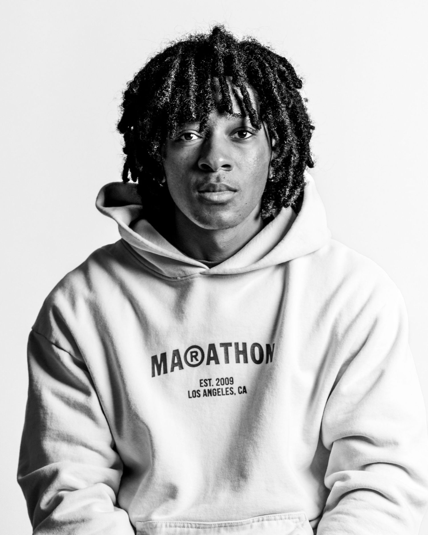 A person in a white Marathon hoodie poses for a black and white portrait.