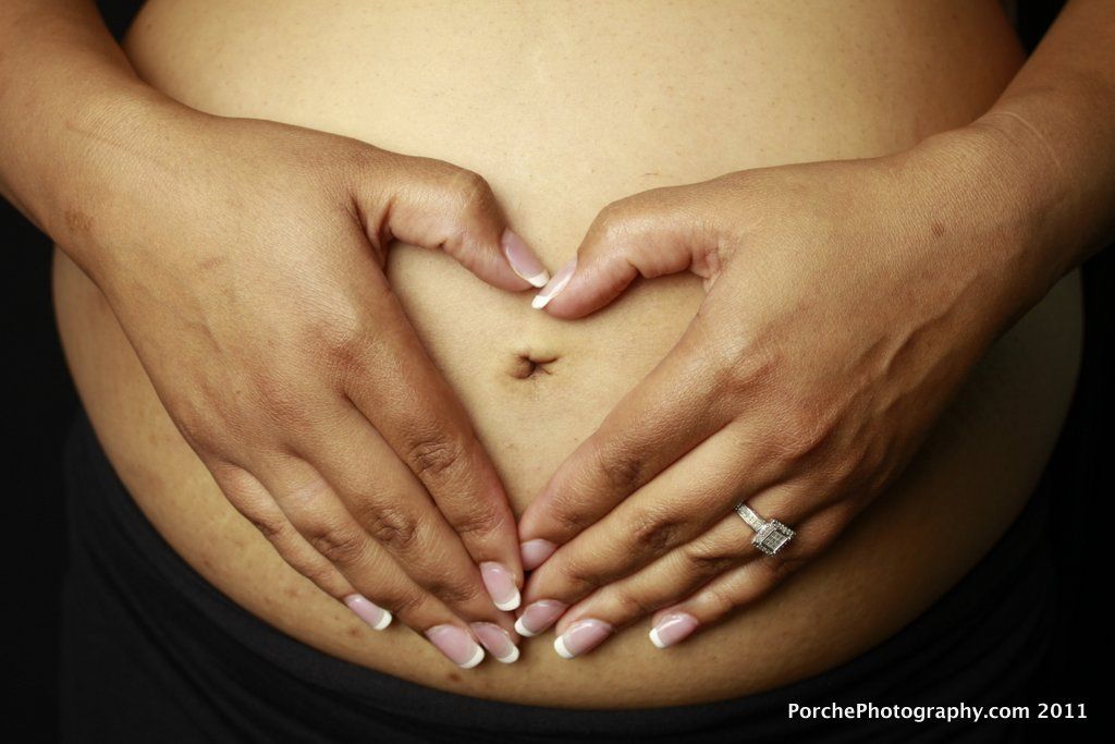 Hands form a heart shape over a pregnant belly while wearing a wedding ring, highlighting the maternal bond.
