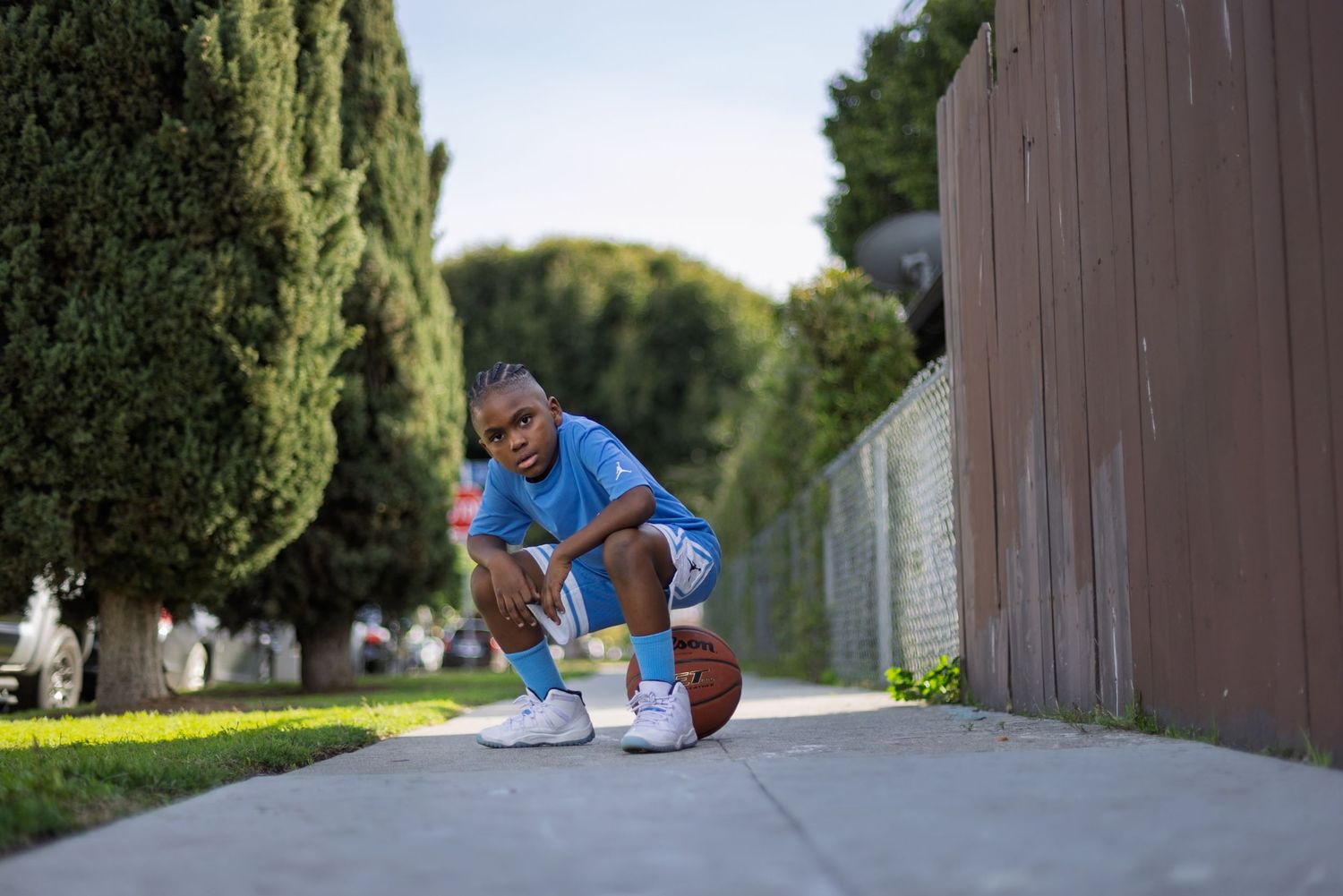 A person in blue athletic wear practices basketball tricks on a concrete path near a brown wall.