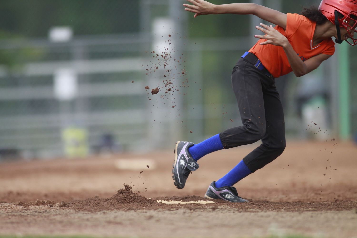 Baseball player slides into base during game creating cloud of dirt on field.